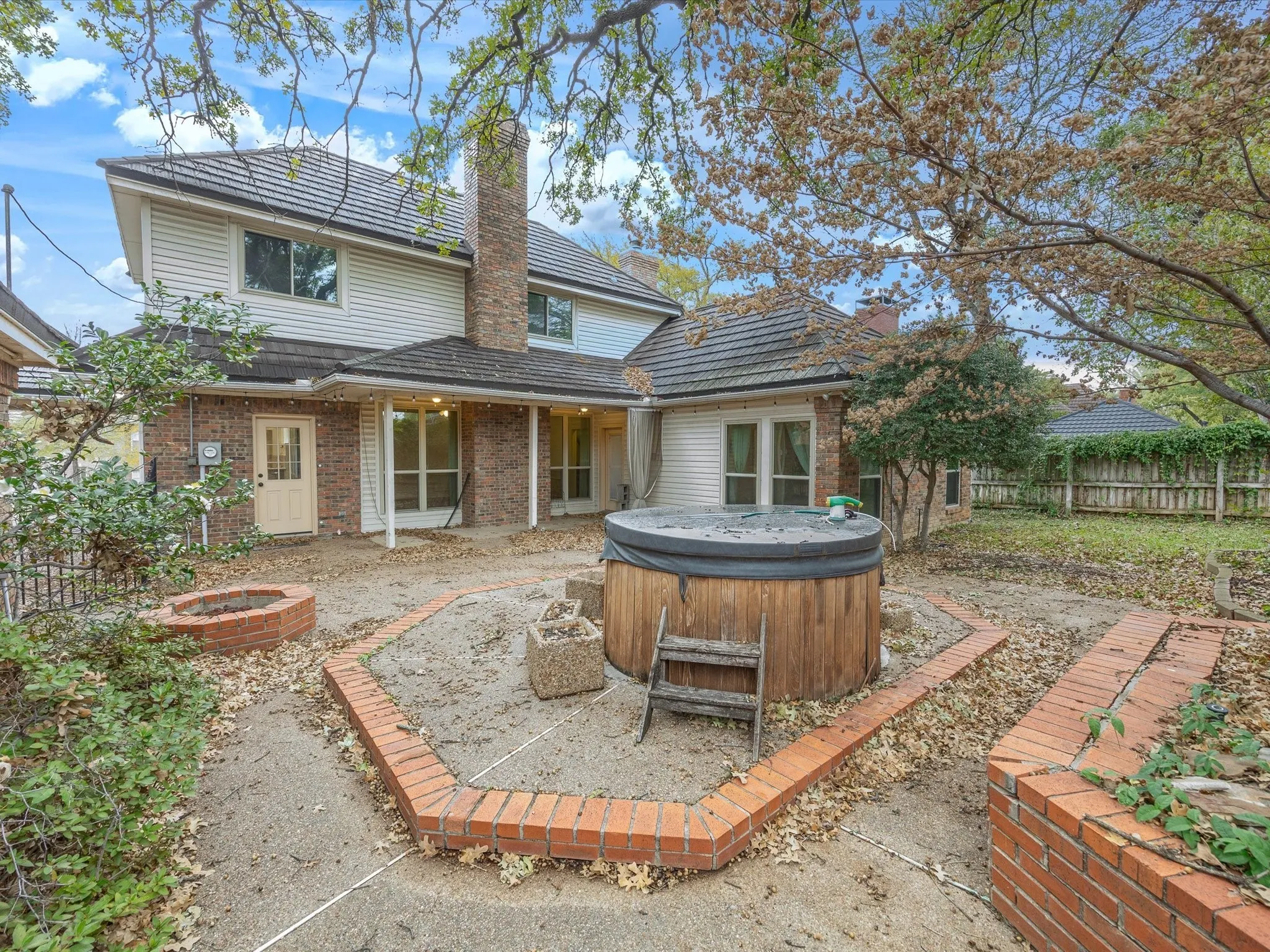 Rear view of property with a patio area, a fenced backyard, a hot tub, brick siding, and a chimney