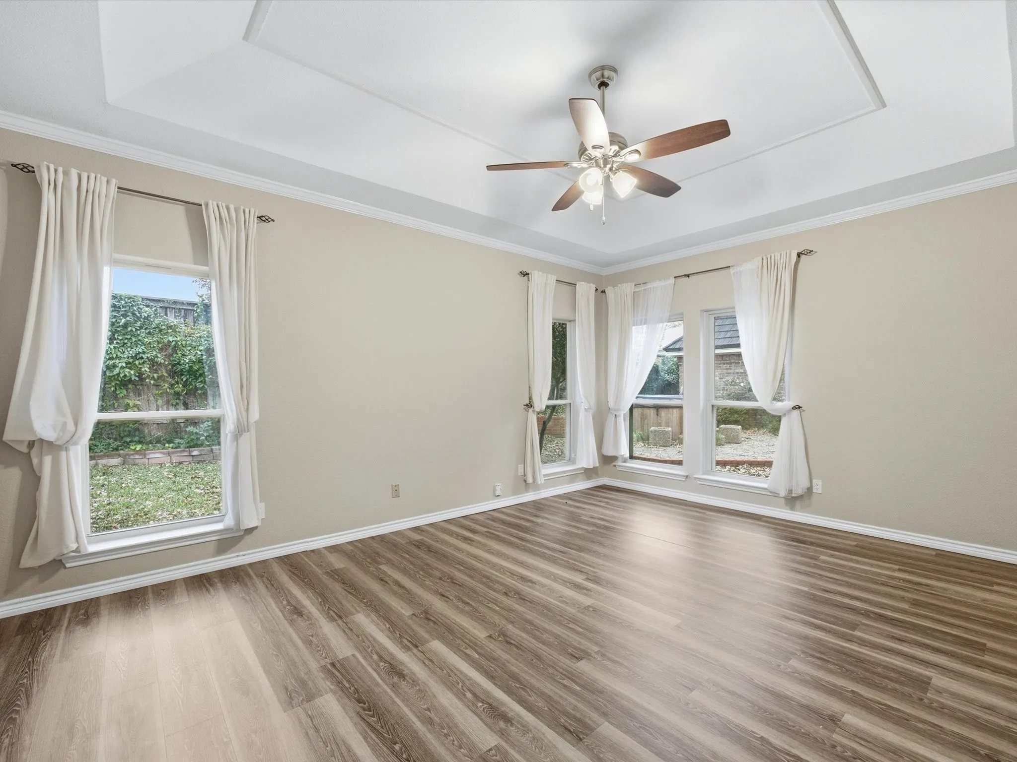 Primary bedroom with a raised ceiling, plenty of natural light, crown molding, and wood finished floors