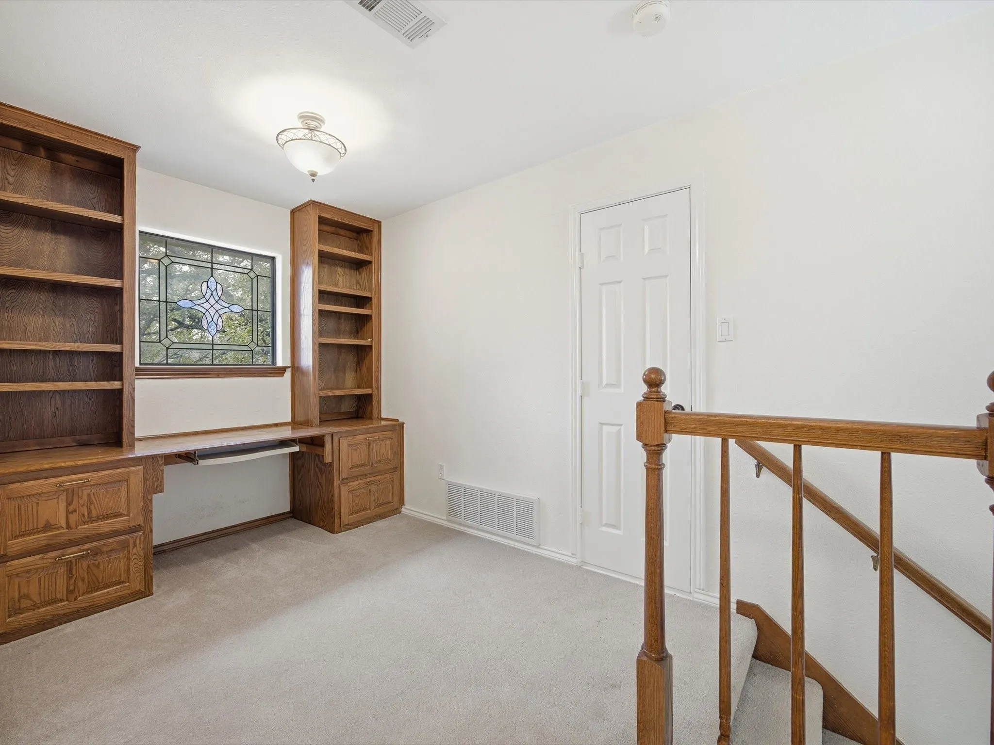 Loft featuring built in desk and light carpet