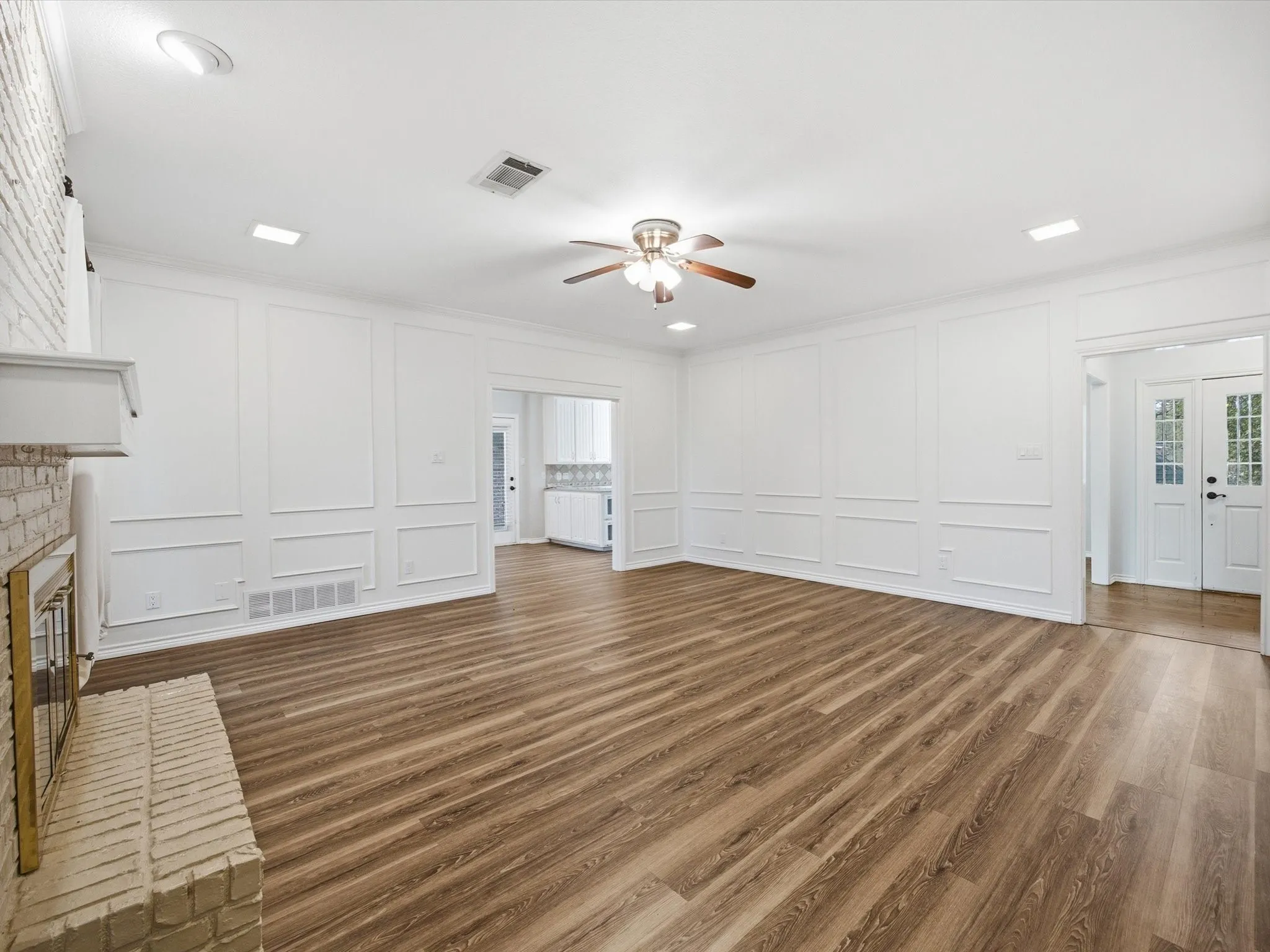 Unfurnished living room featuring a decorative wall, dark wood-style flooring, a brick fireplace, ceiling fan, and french doors