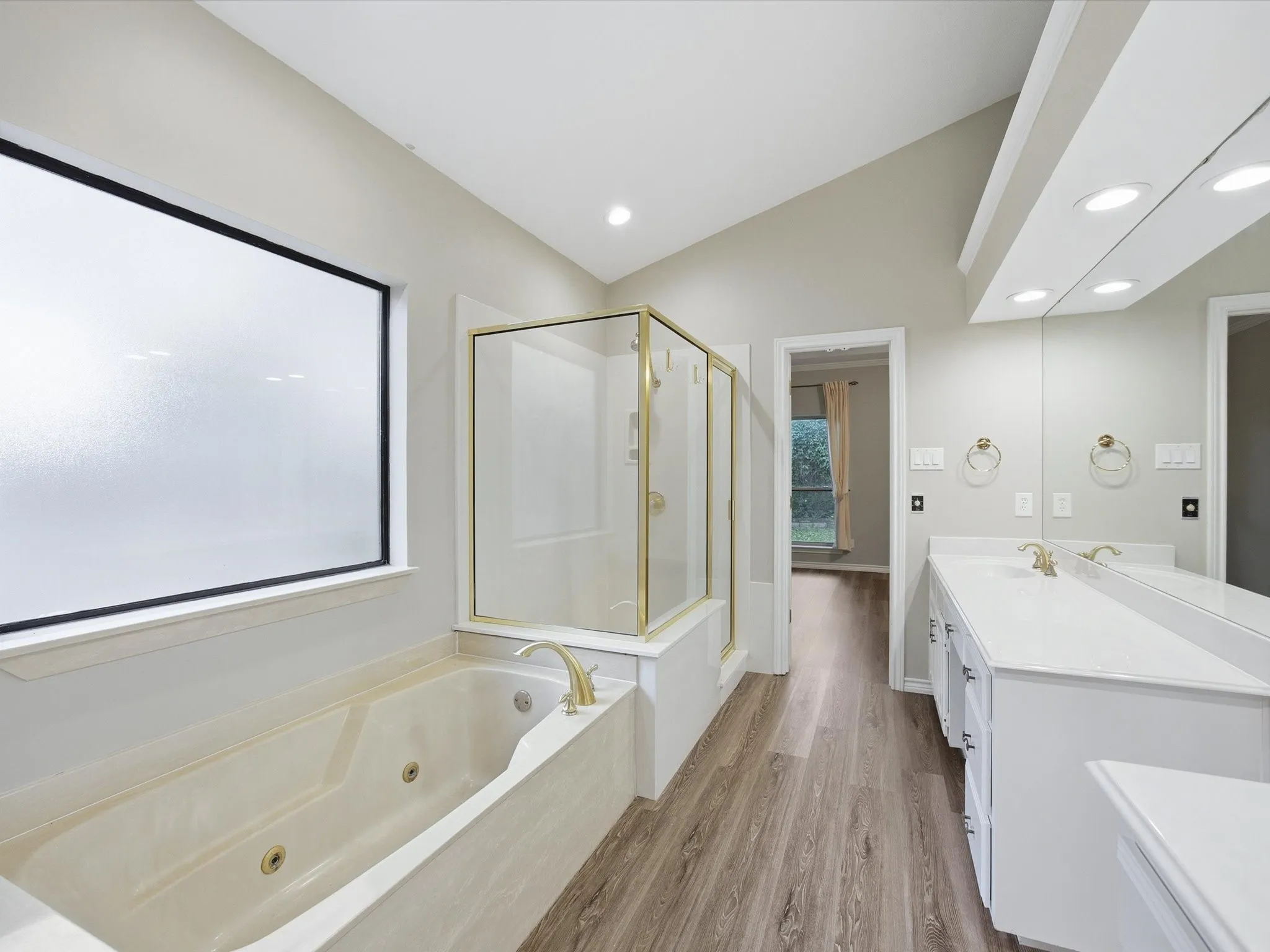 Primary bathroom featuring a stall shower, light wood finished floors, vanity, a jetted tub, and vaulted ceiling