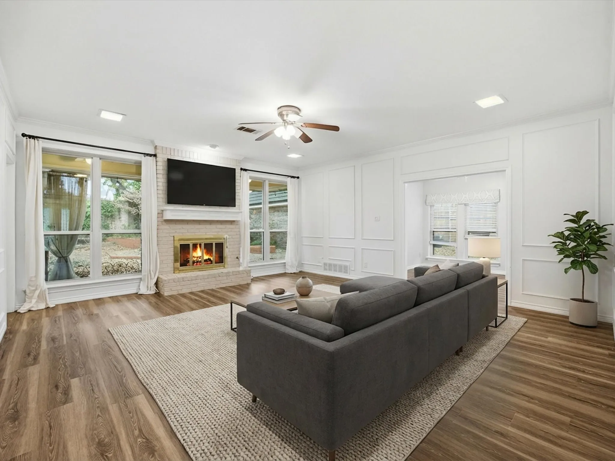 Living room with a decorative wall, healthy amount of natural light, ceiling fan, ornamental molding, and wood finished floors