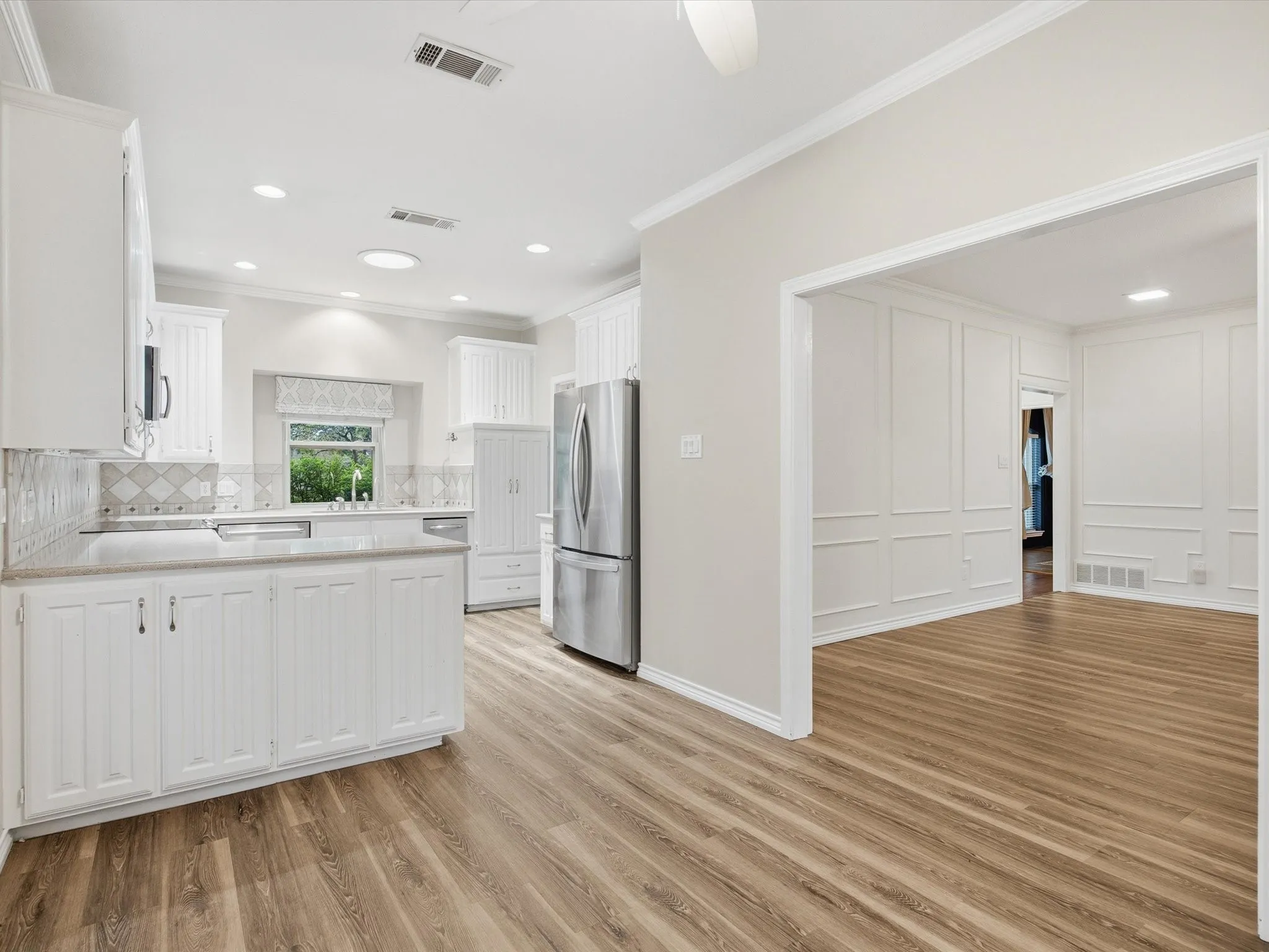 Kitchen with white cabinets, light wood-style flooring, backsplash, freestanding refrigerator, and a peninsula
