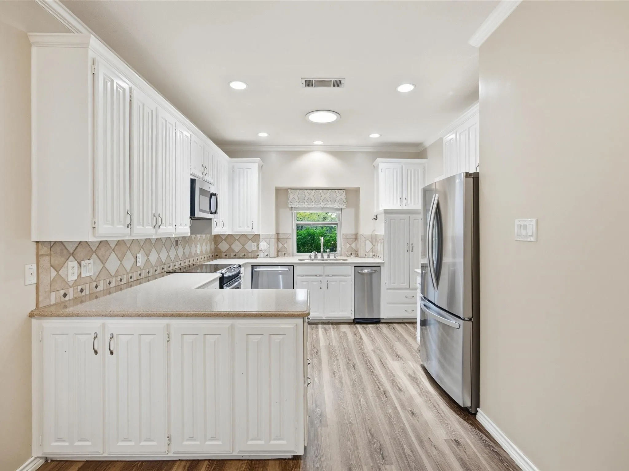 Kitchen with a peninsula, white cabinets, crown molding, appliances with stainless steel finishes, and tasteful backsplash