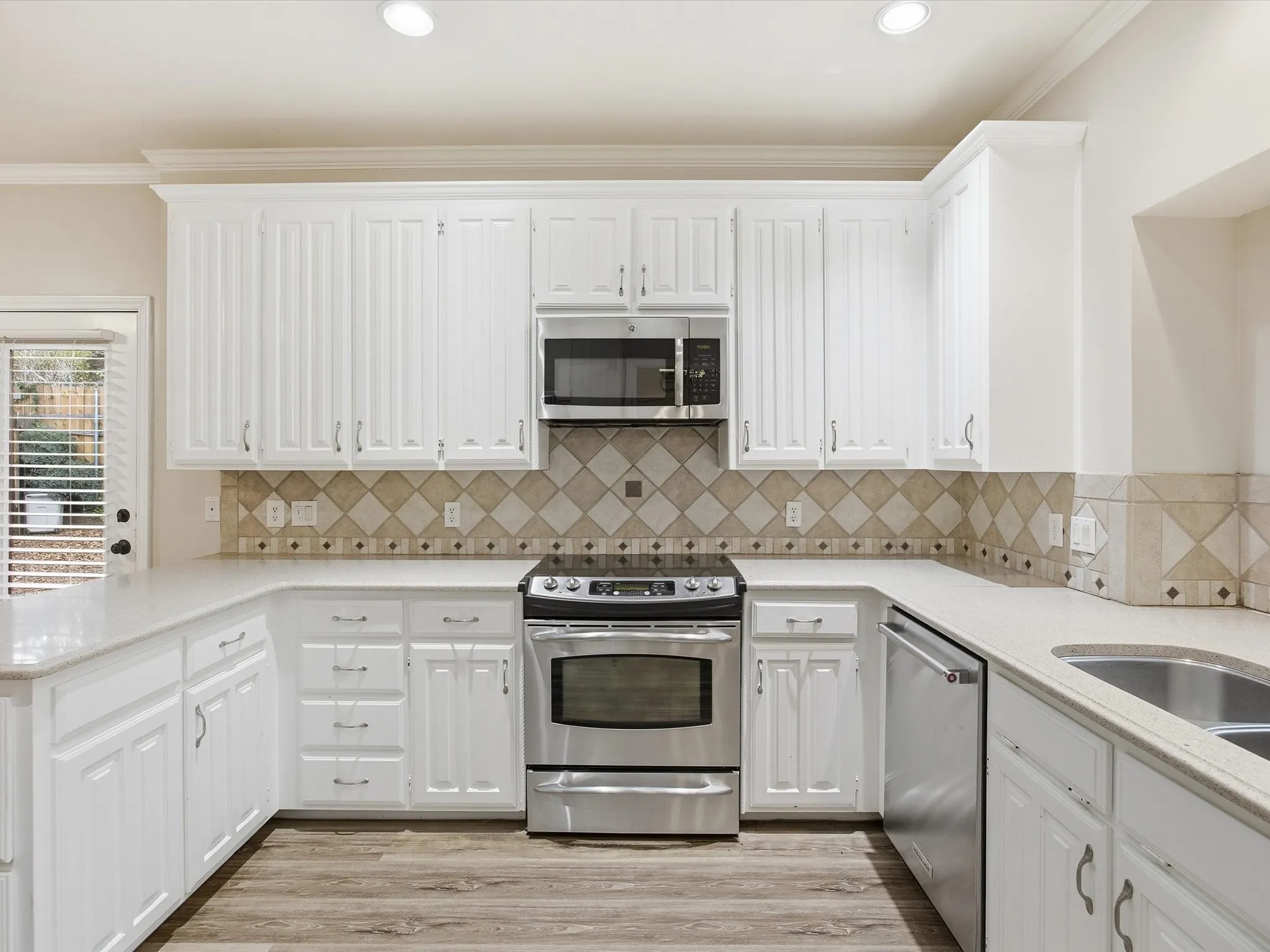 Kitchen featuring appliances with stainless steel finishes, white cabinetry, backsplash, crown molding, and light stone counters