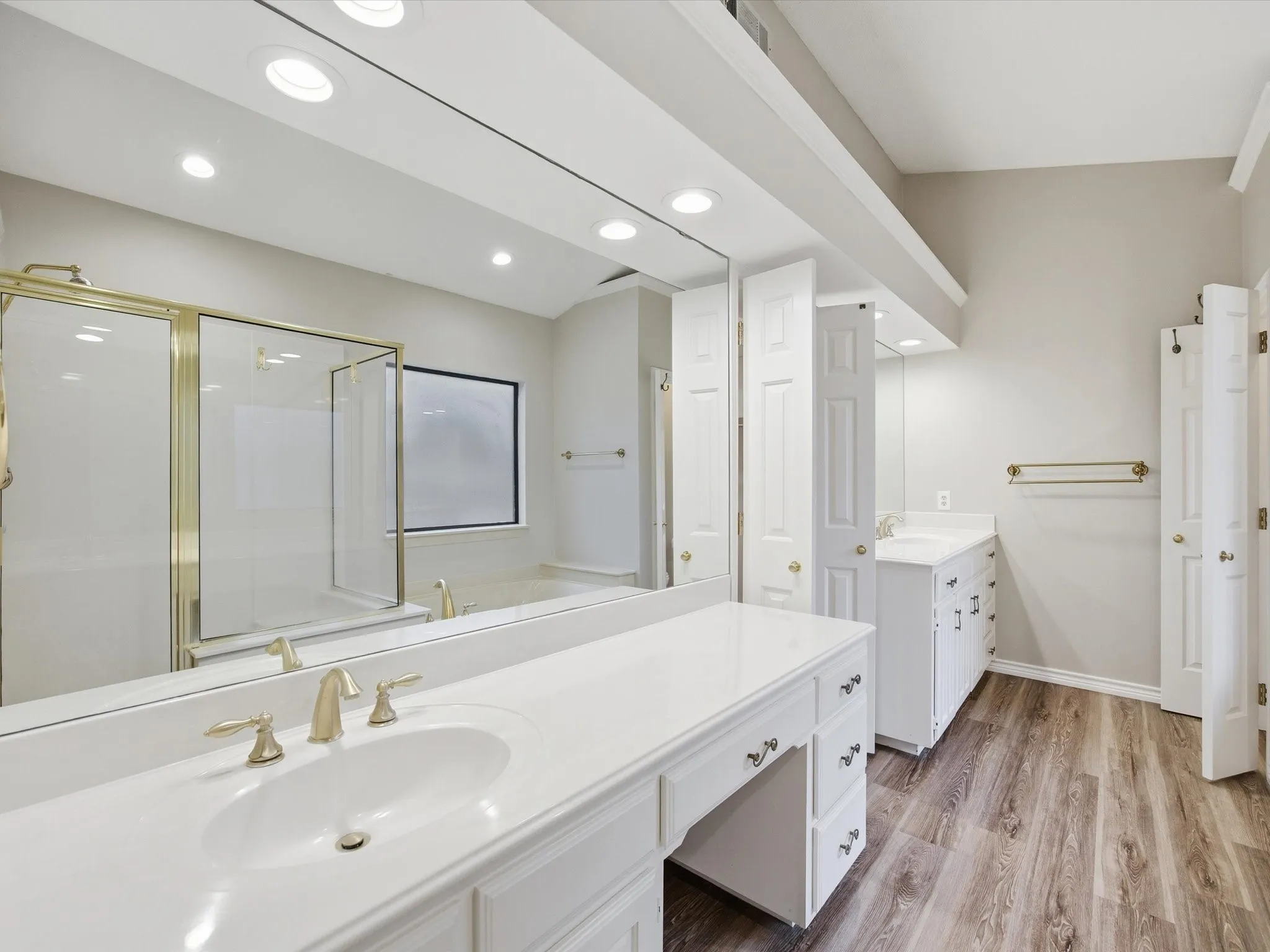 Primary bath featuring a stall shower, two vanities, light wood-type flooring, recessed lighting, and a bath