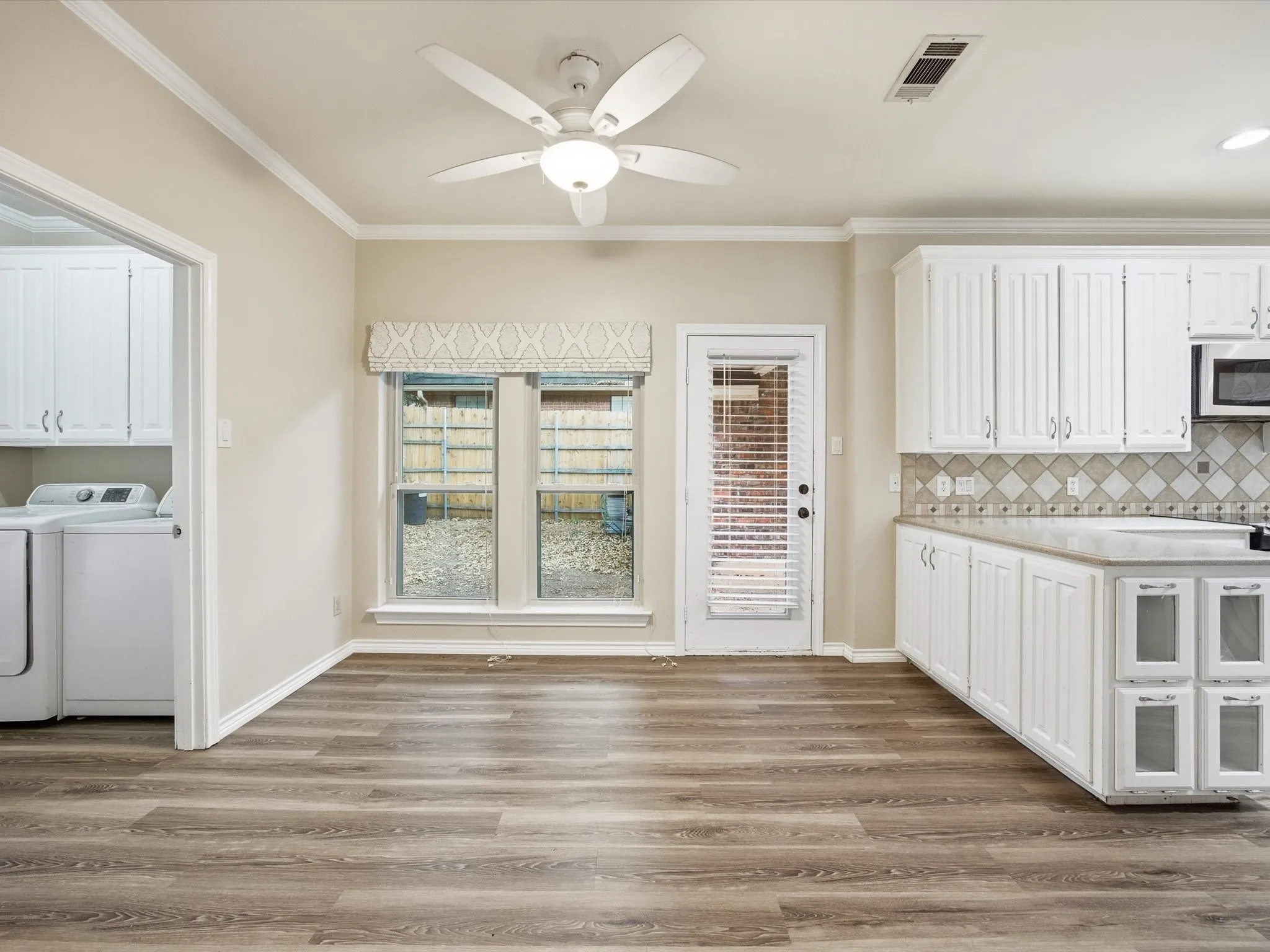 Kitchen with white cabinets, ornamental molding, light wood-style flooring, and ceiling fan