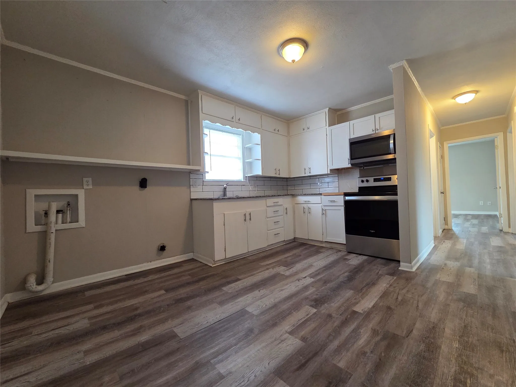 Kitchen featuring stainless steel appliances, ornamental molding, white cabinets, dark wood-style flooring, and light countertops