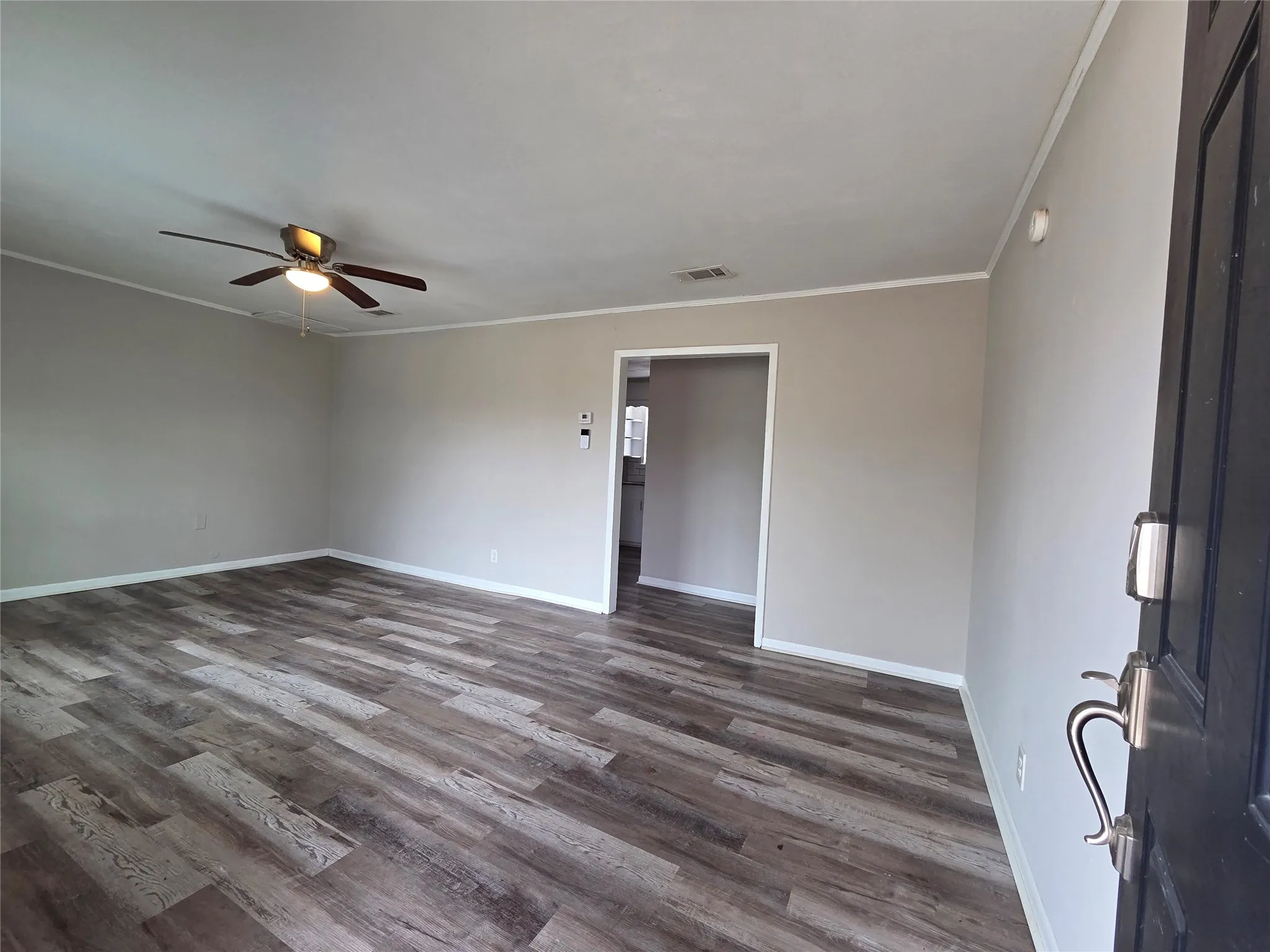Living room with dark wood-style flooring, ornamental molding, and a ceiling fan from the front door.