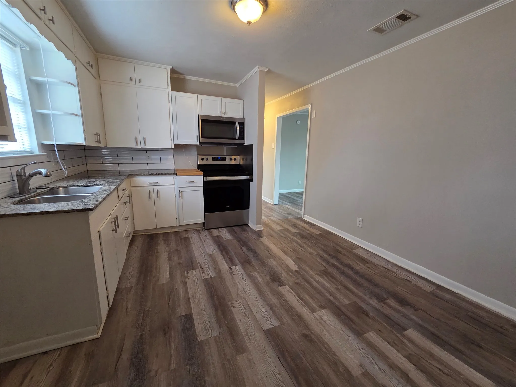 Kitchen featuring stainless steel appliances, backsplash, dark wood finished floors, ornamental molding, and open shelves