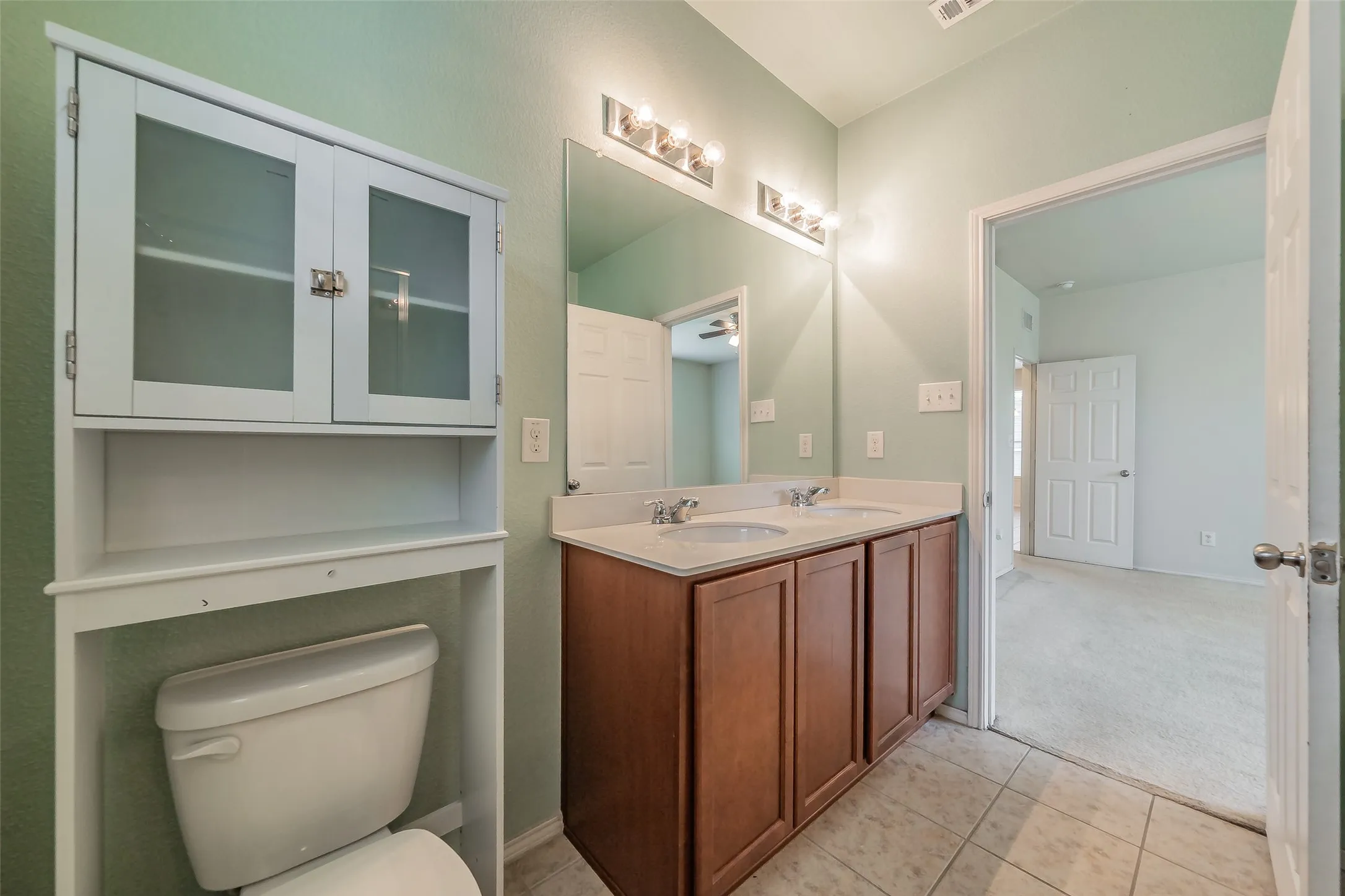 Bathroom featuring a double vanity with wood-finish cabinetry, a large mirror, and overhead light fixtures