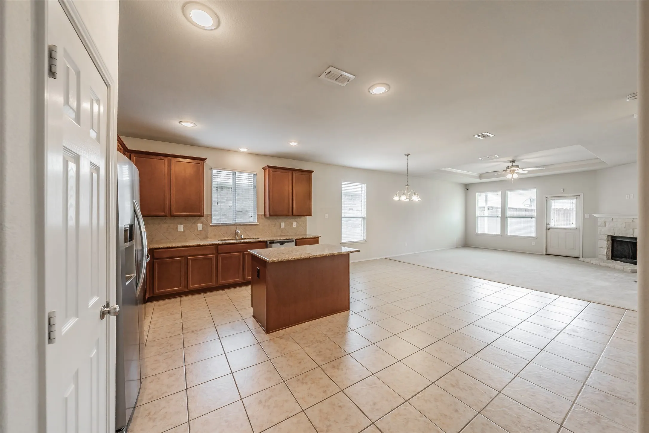 Open-concept living space with a kitchen island, recessed lighting, tile flooring, a tray ceiling, and a stone-surround fireplace