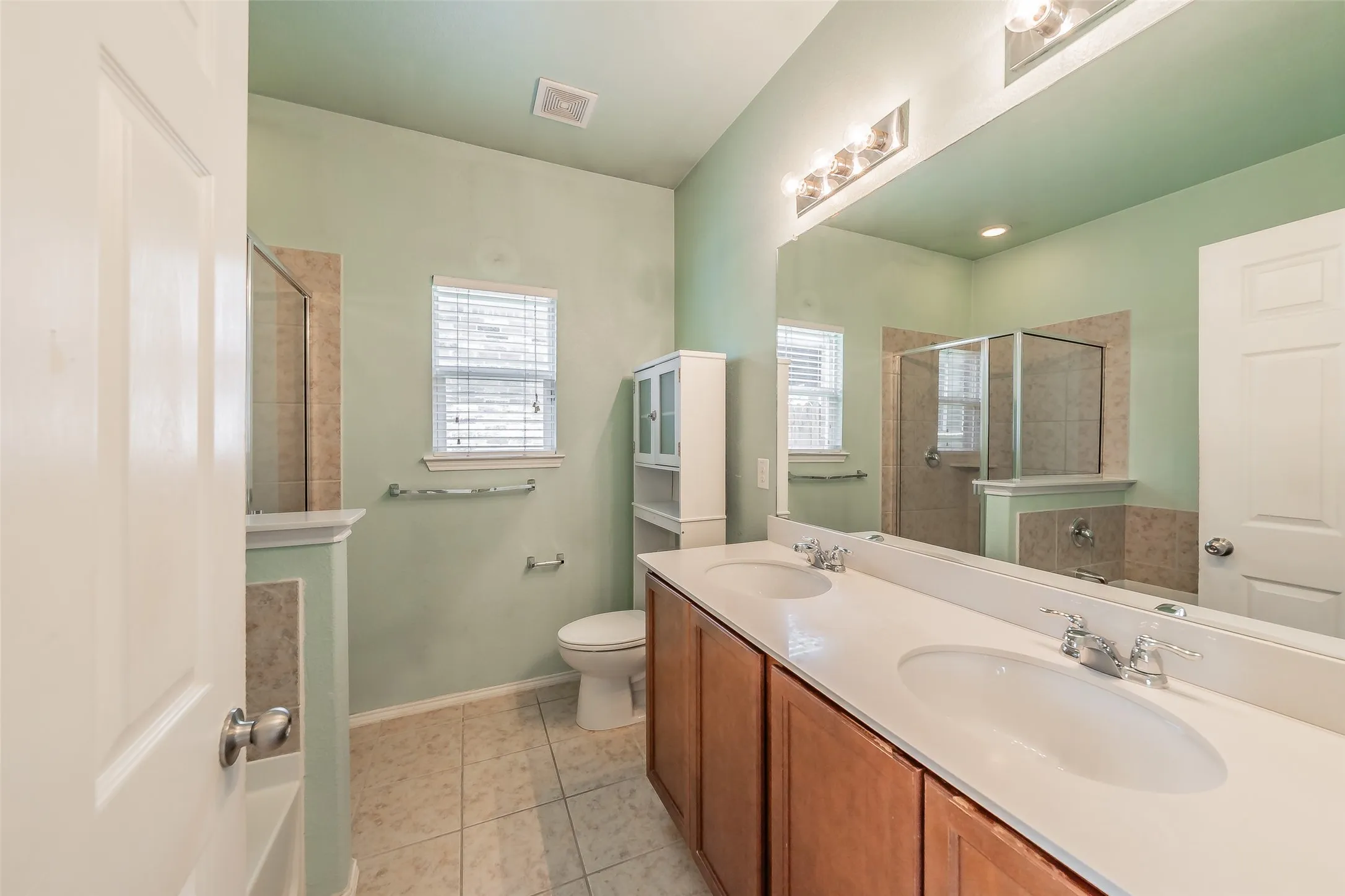Double vanity with integrated sinks, wood cabinetry, and an expansive mirror