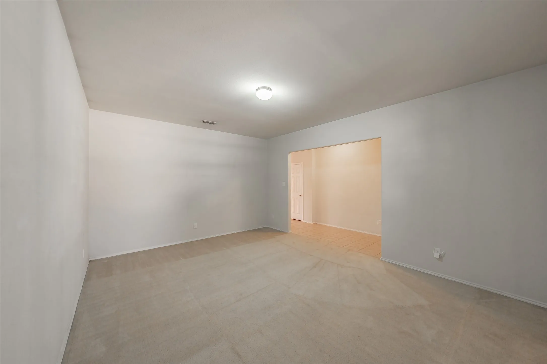 Spacious living area featuring light gray wall paint, neutral carpeting, and a recessed ceiling light fixture