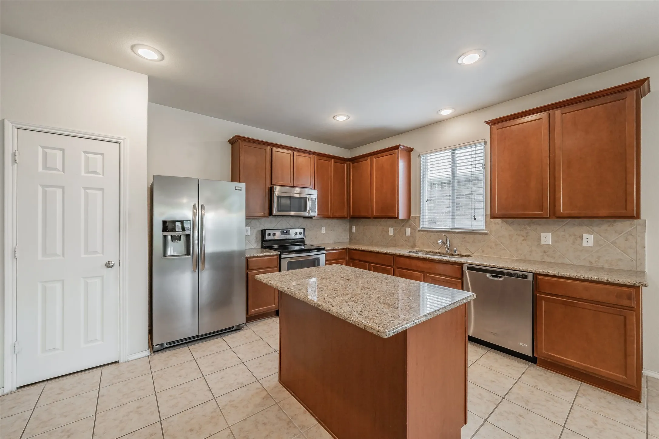 Kitchen featuring an island with stone countertop, stainless steel appliances, wood cabinetry, tile flooring, and recessed lighting
