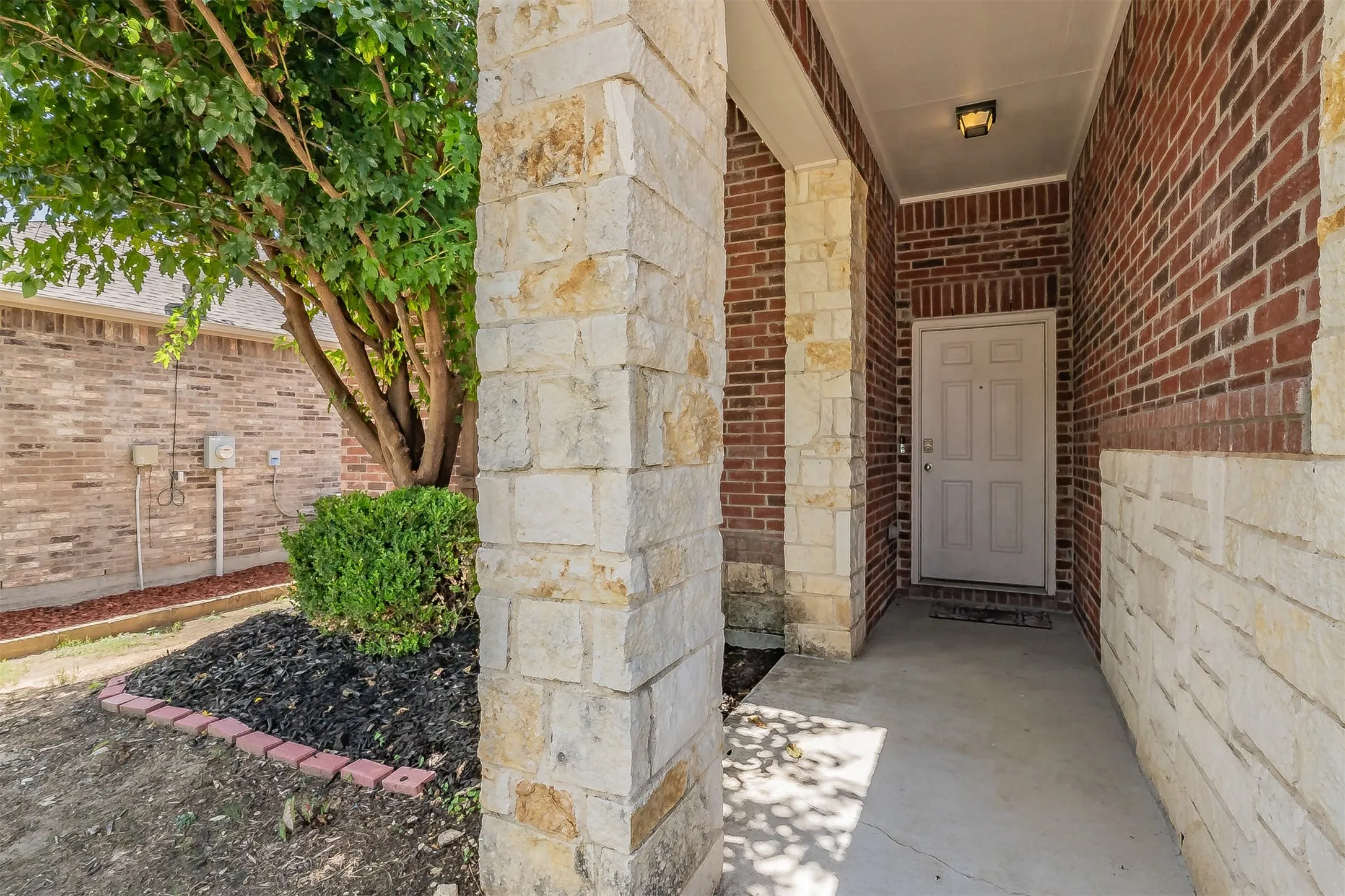 Entryway featuring brick and stone veneer, a covered porch with a paneled door, and an exterior light fixture