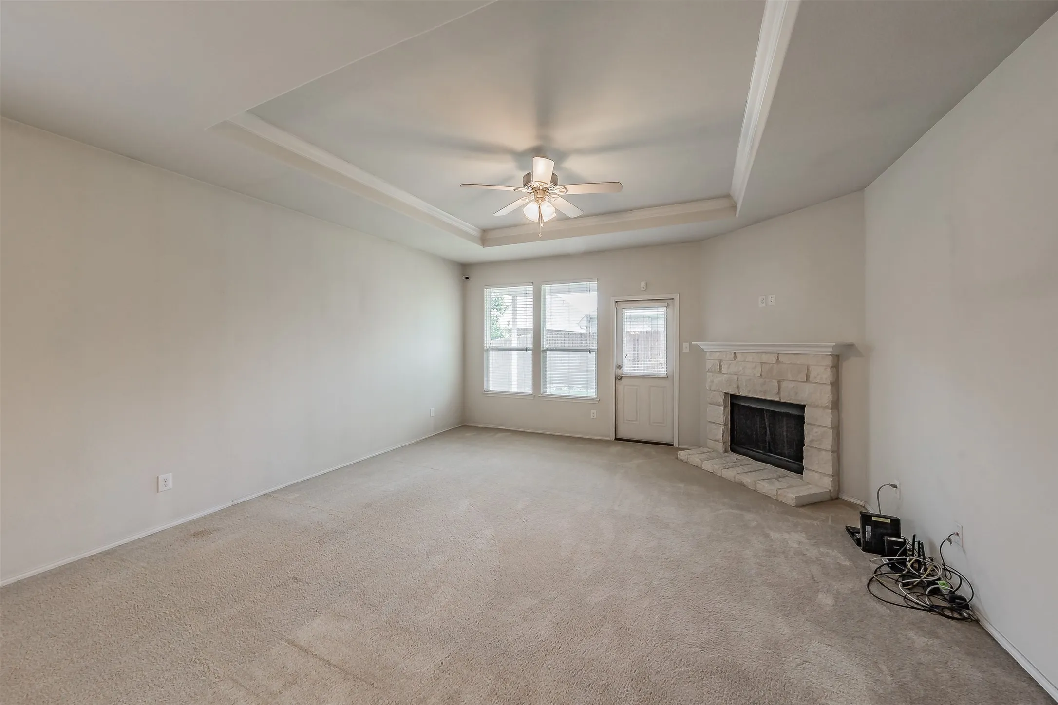 Spacious room featuring tray ceilings, a ceiling fan, and carpet flooring