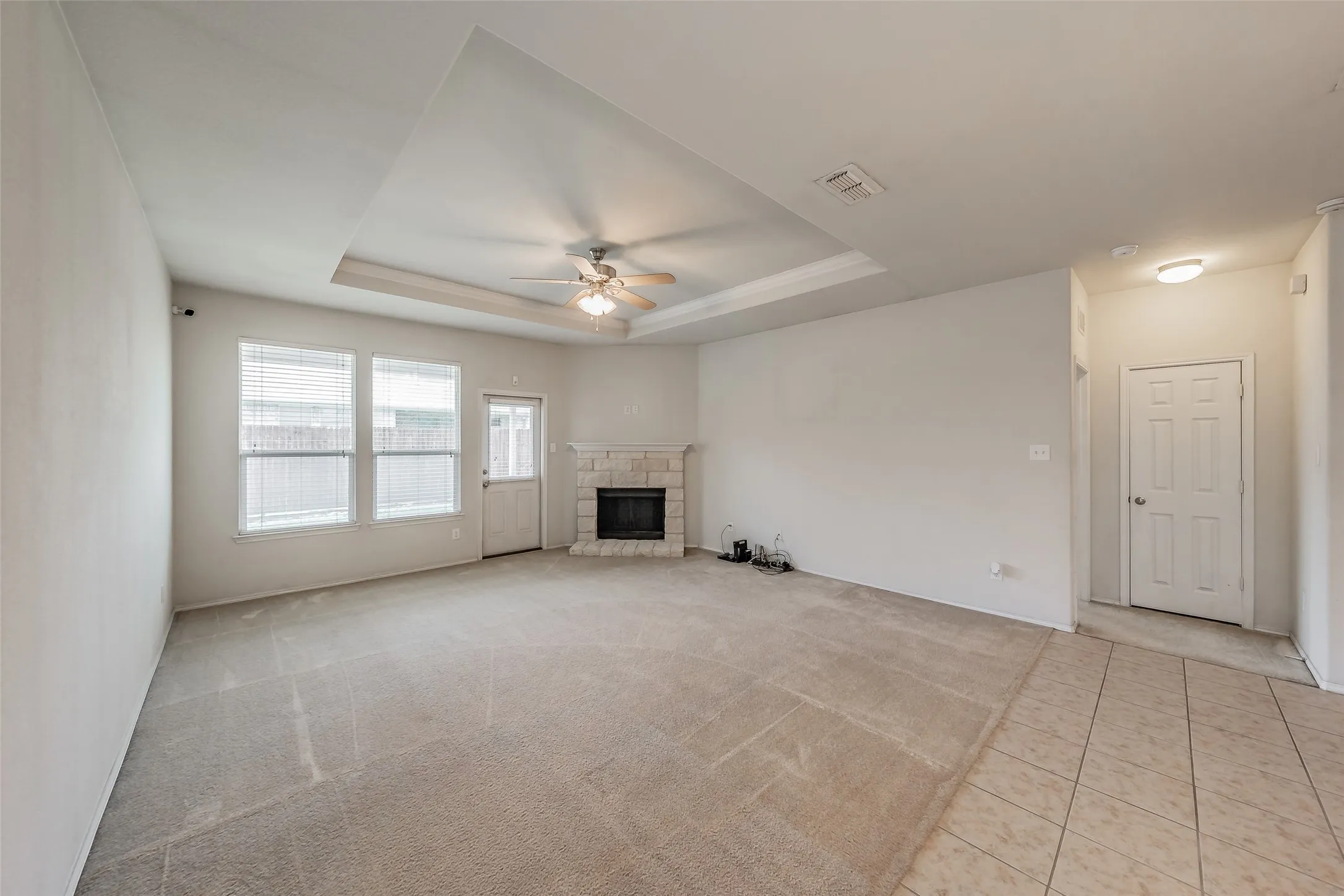 Living area featuring a stone-clad fireplace and a tray ceiling with a ceiling fan