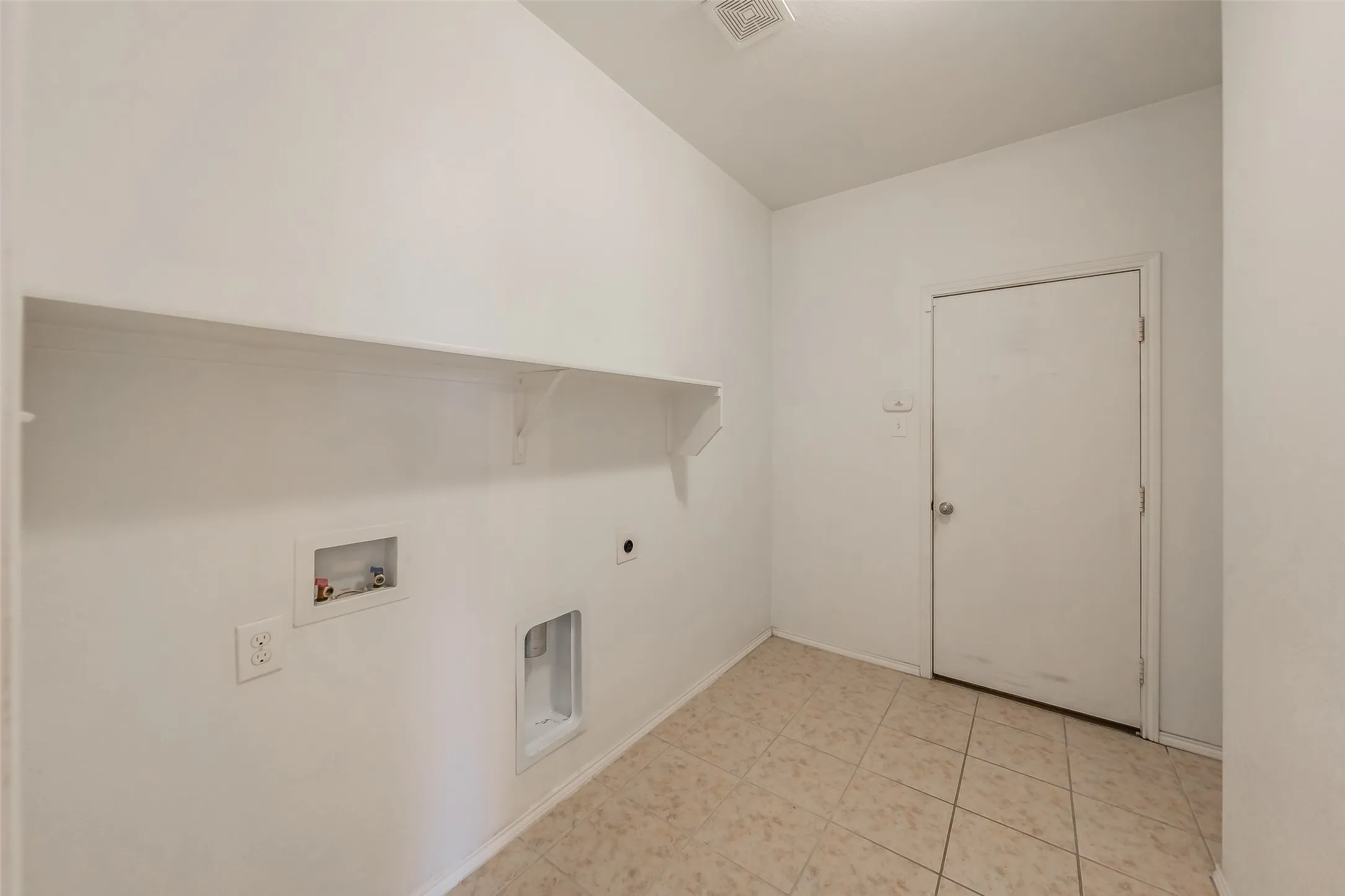 Laundry area featuring a built-in shelf, white walls, light-toned tile flooring, and a standard white door