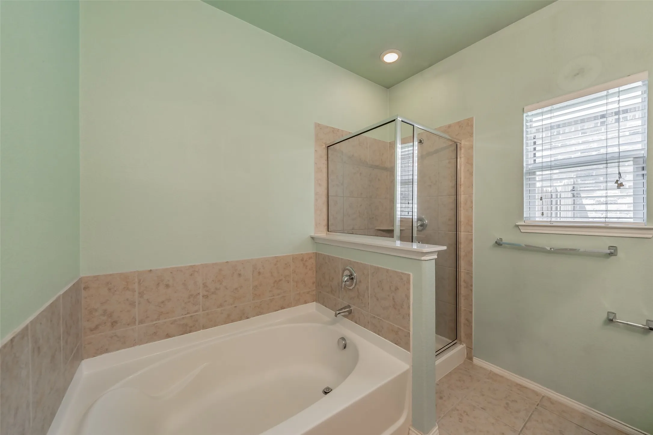 Bathroom with a built-in soaking tub, a tiled shower enclosure with glass doors, and a window with blinds