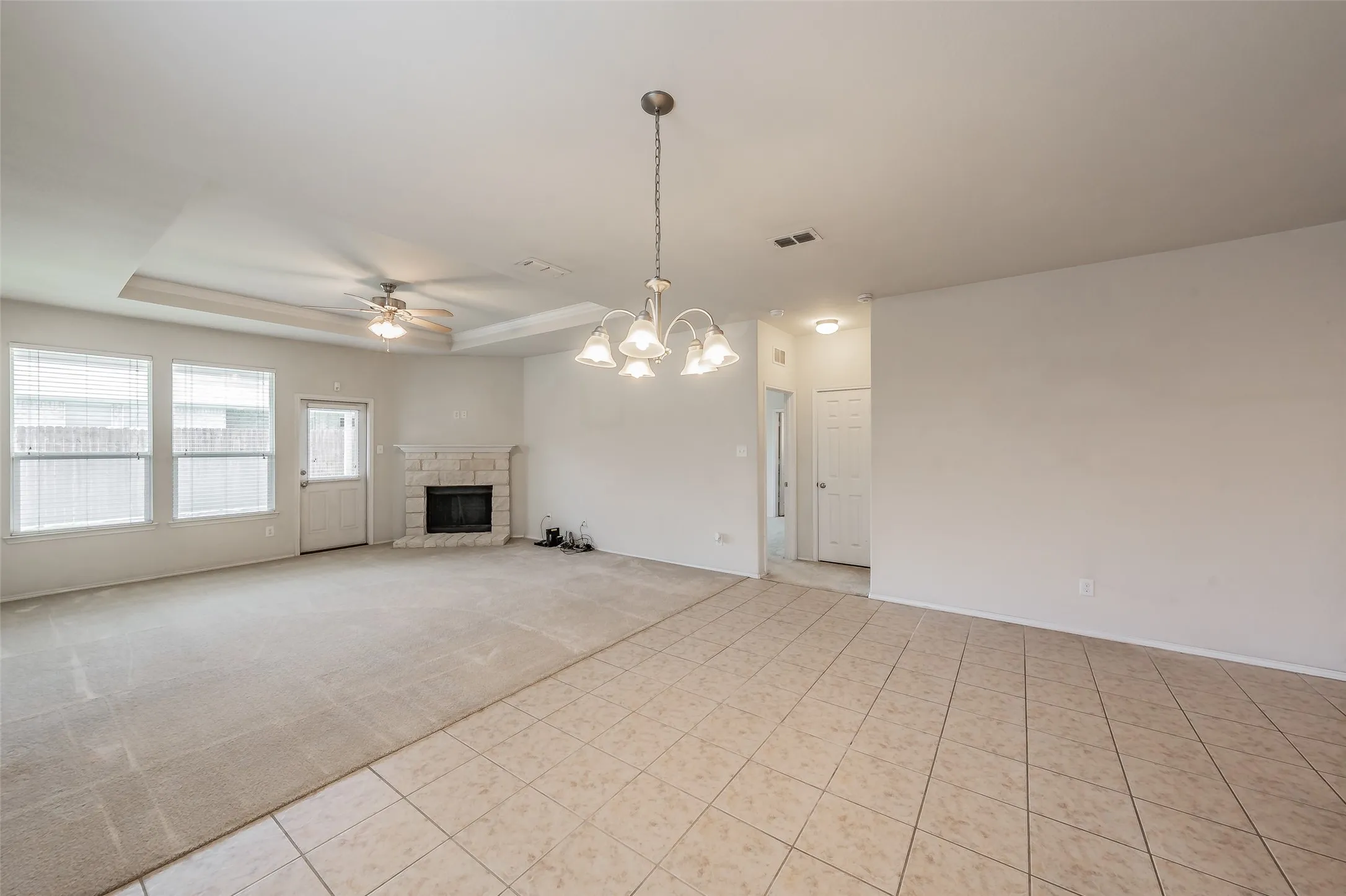 Expansive living area featuring a stone-clad fireplace and tray ceiling with a ceiling fan