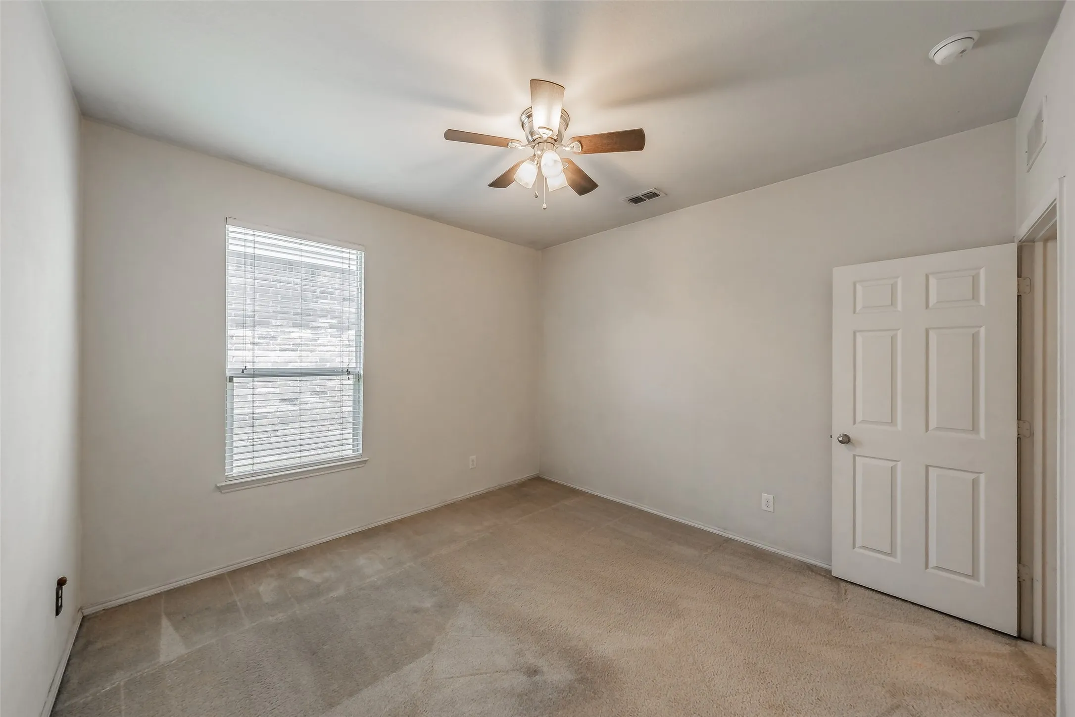 Carpeted room featuring a single window with blinds, a ceiling fan with integrated lighting, and a six-panel interior door