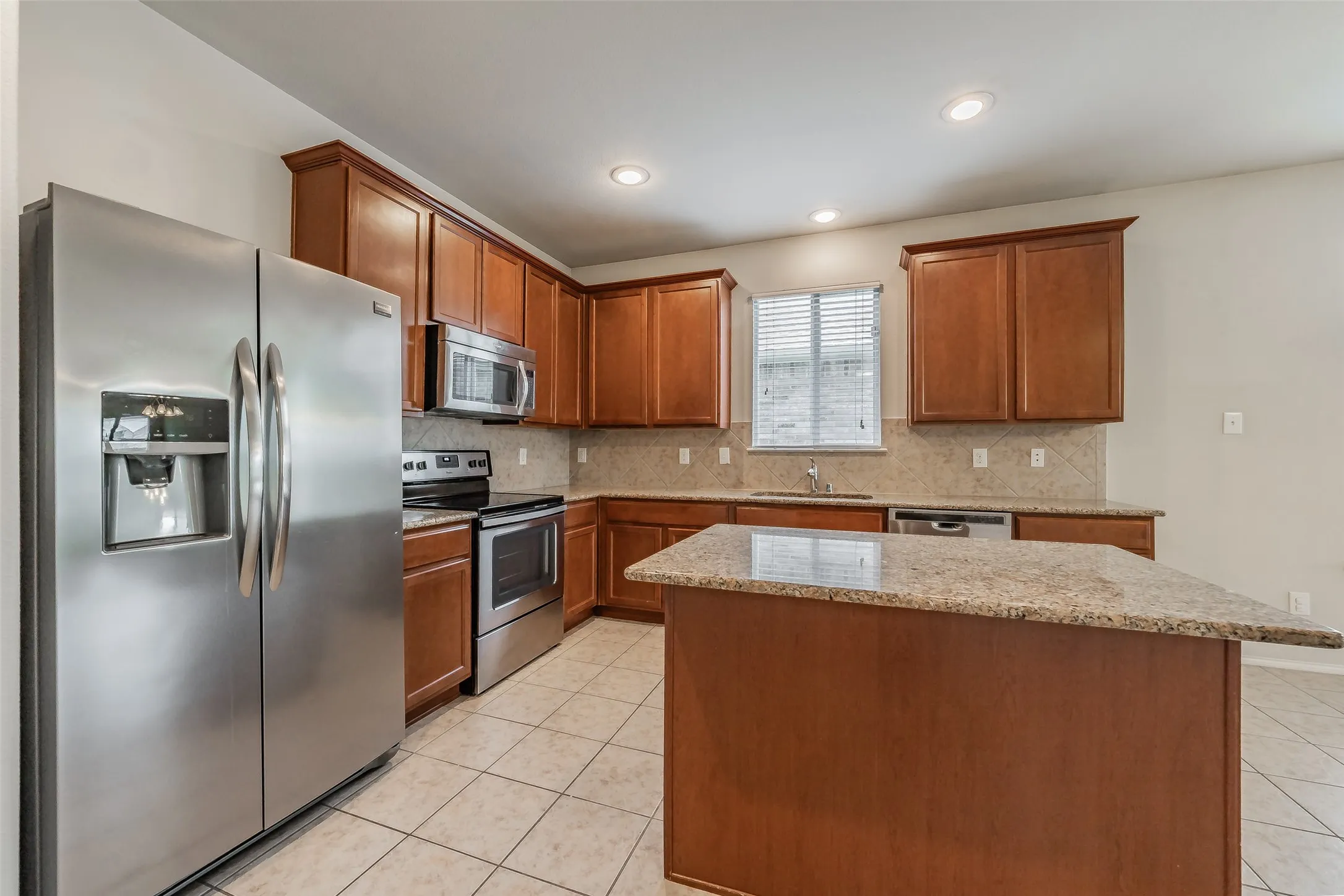 Kitchen featuring an island with stone countertop, stainless steel appliances, wood cabinetry, tile flooring, and recessed lighting