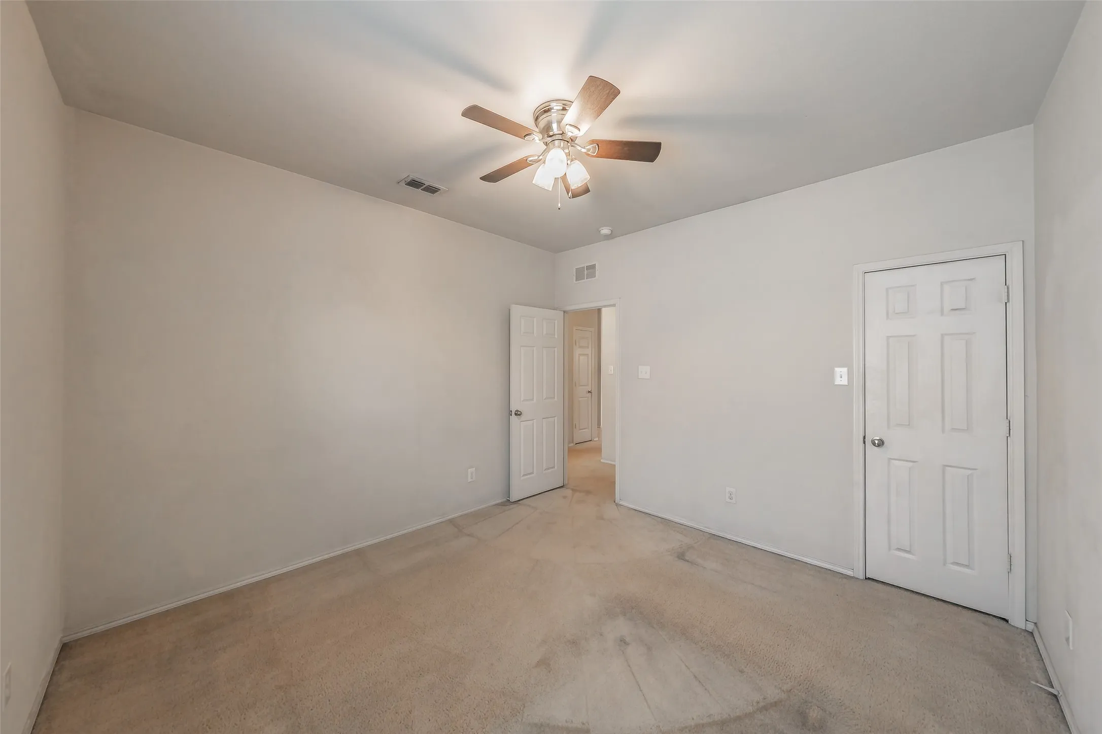 Carpeted room with a ceiling fan light fixture and two paneled doors