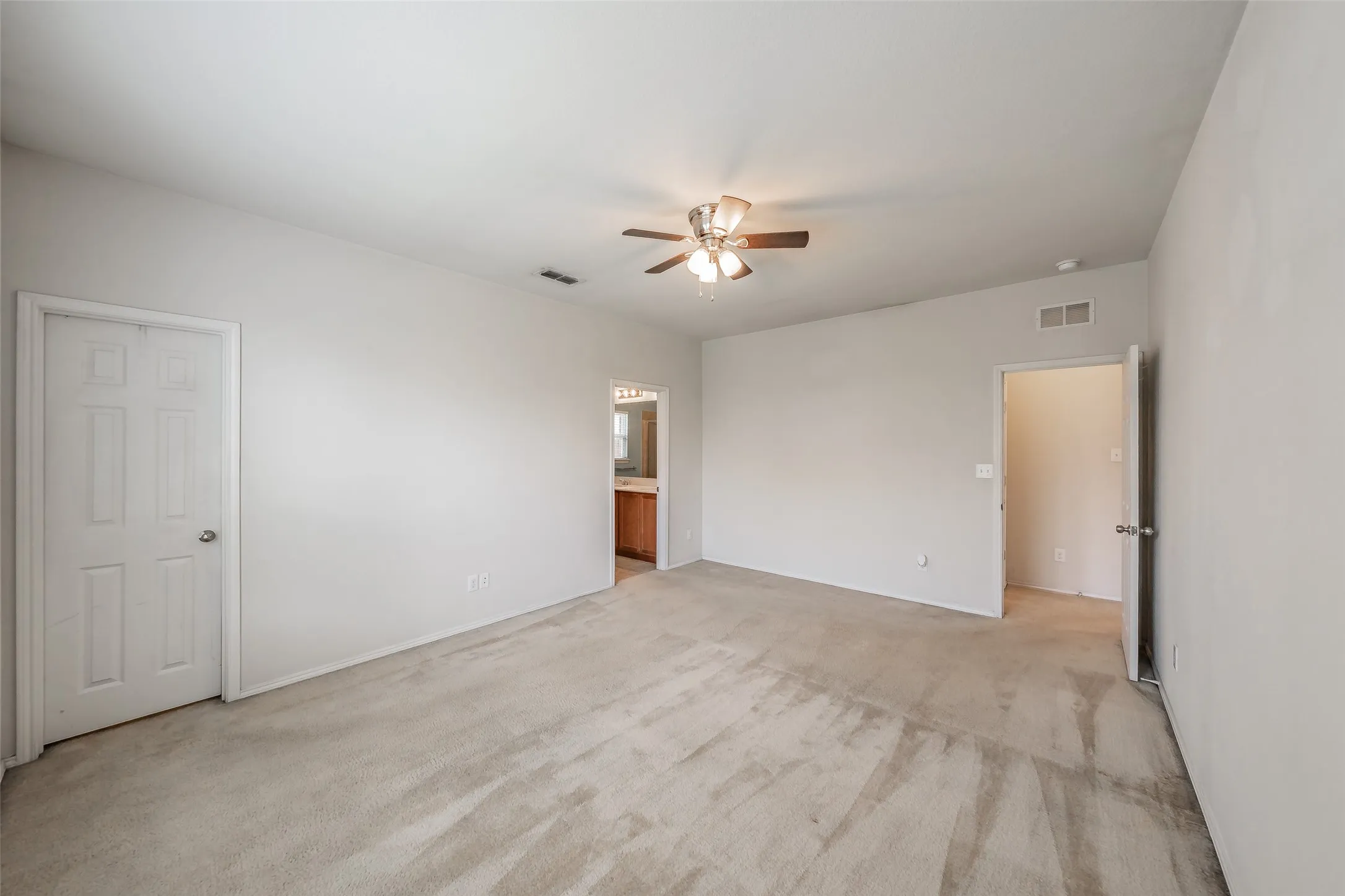 Spacious carpeted room featuring a ceiling fan with integrated lighting, neutral wall paint, and multiple doorways