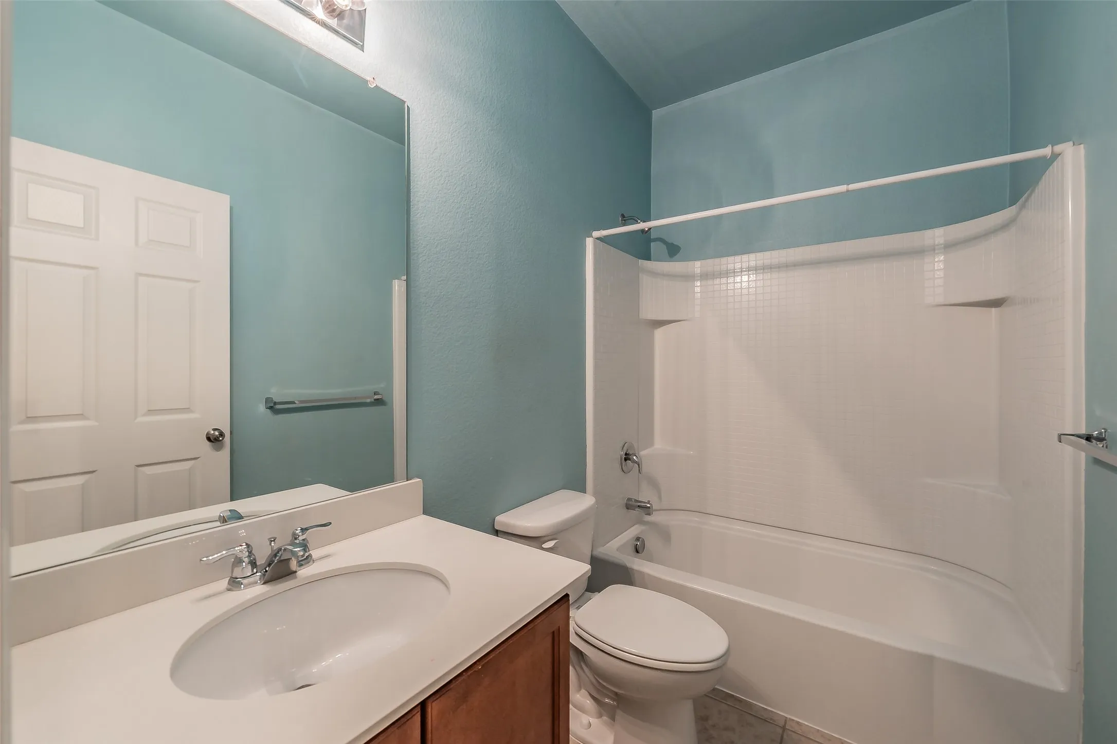 Full bathroom featuring a single vanity with a white countertop and undermount sink, chrome faucet, and wood-finish cabinetry