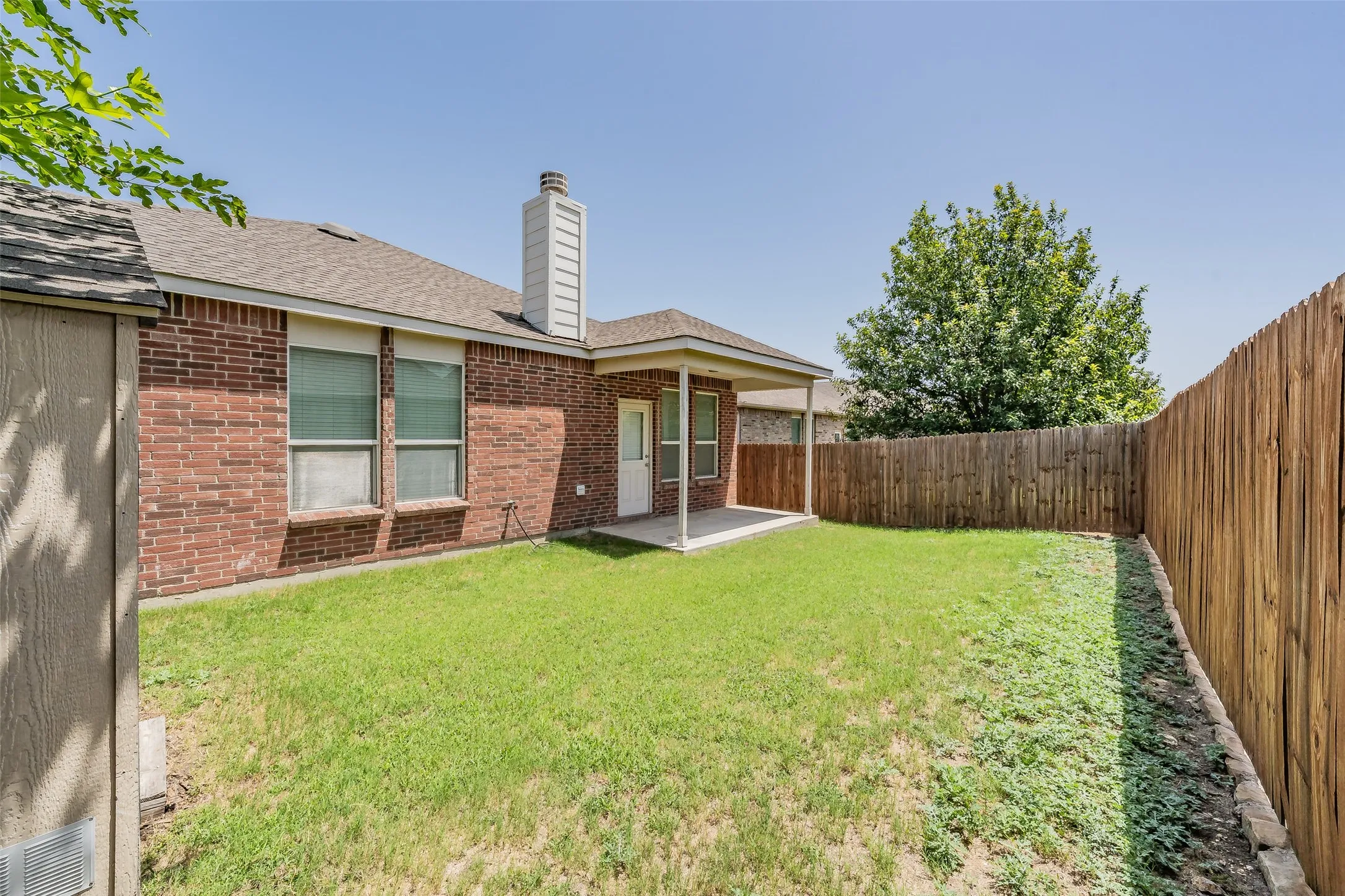 Expansive backyard featuring a manicured lawn, a full wood privacy fence, and a covered patio