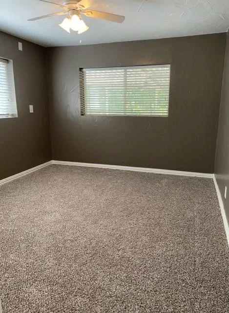 Spacious room featuring neutral wall paint, two windows with blinds, a ceiling fan with integrated lighting, and plush carpet flooring