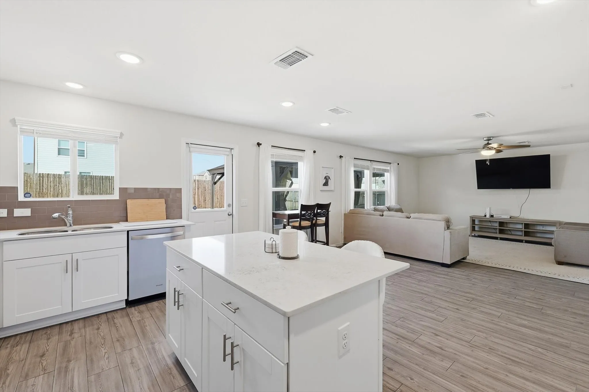 Kitchen with white cabinetry, tasteful backsplash, a kitchen island, dishwasher, and open floor plan