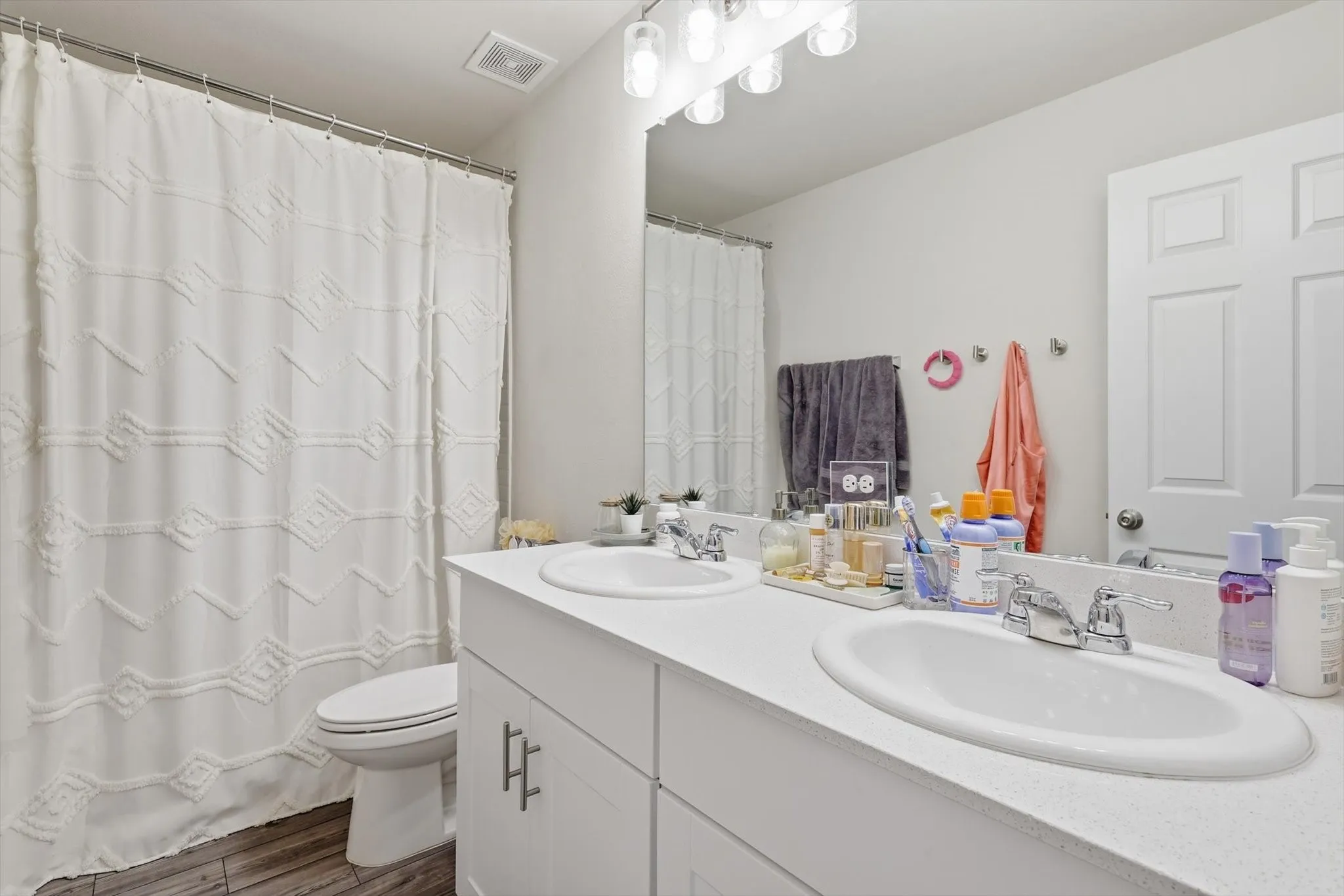 Full bath with double vanity and dark wood-type flooring