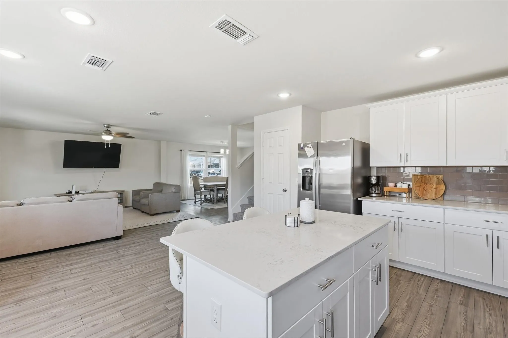 Kitchen with white cabinetry, a kitchen island, stainless steel refrigerator with ice dispenser, backsplash, and open floor plan