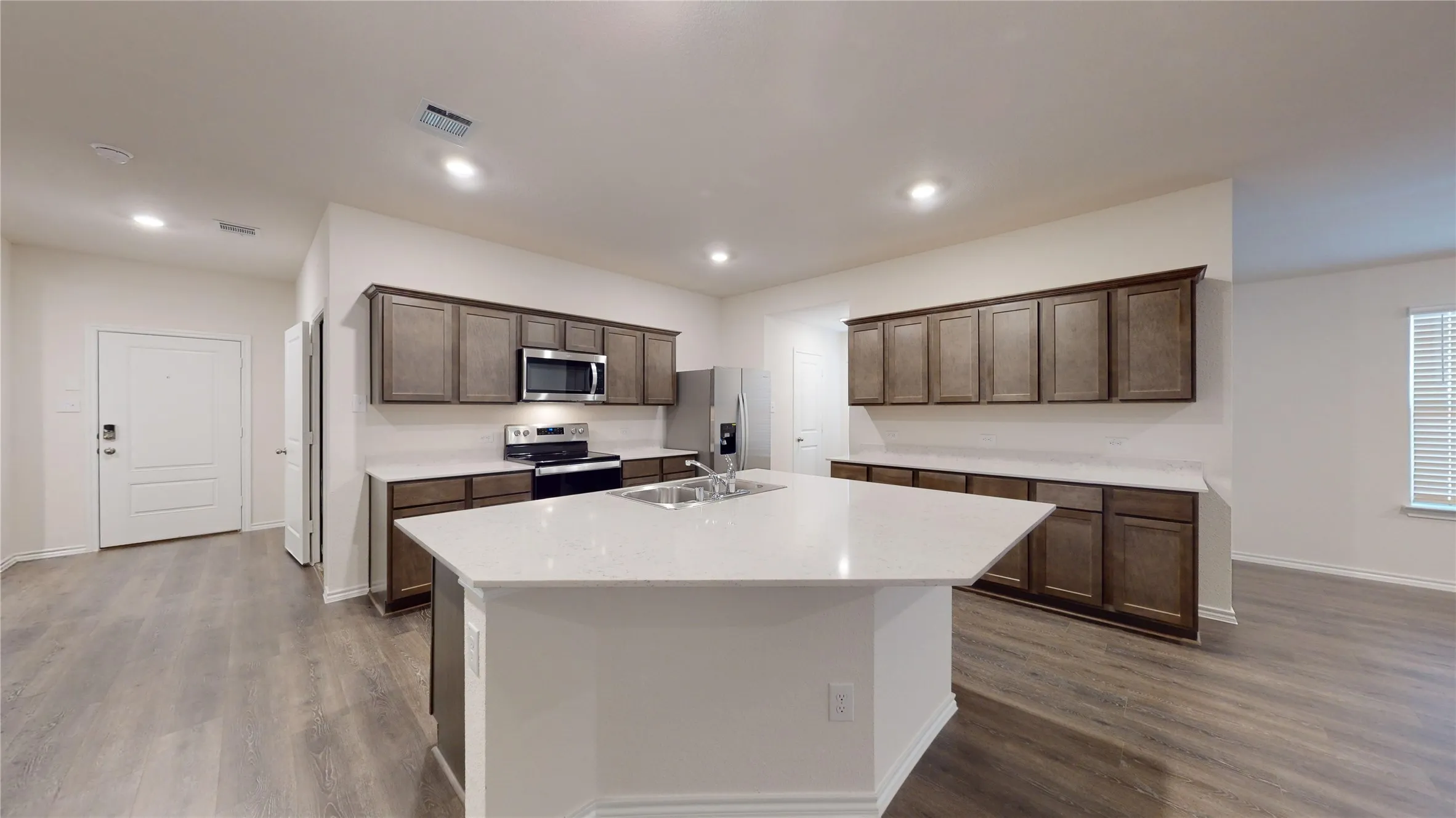 Kitchen featuring stainless steel appliances, an island with sink, dark wood-type flooring, dark brown cabinets, and recessed lighting