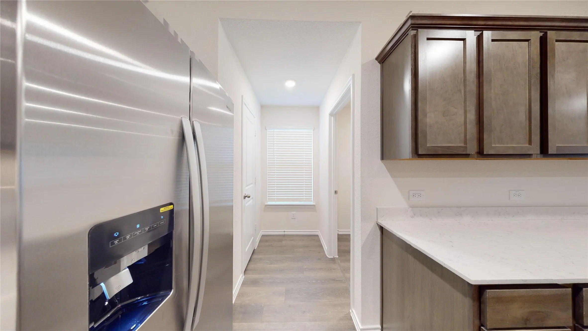 Kitchen featuring stainless steel fridge, dark brown cabinetry, light wood finished floors, and light stone counters