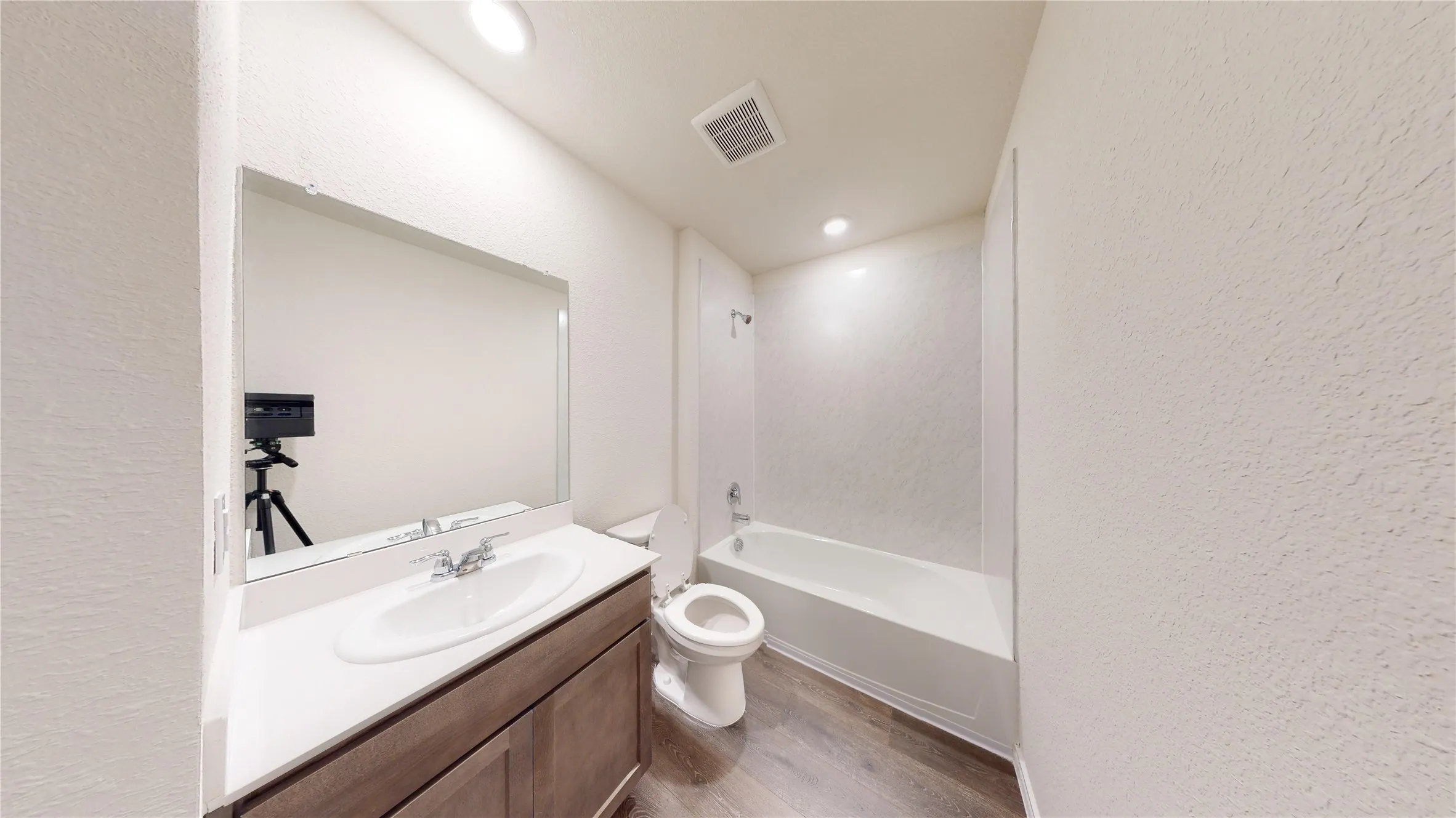 Full bathroom with a textured wall, vanity, washtub / shower combination, light wood-style floors, and recessed lighting