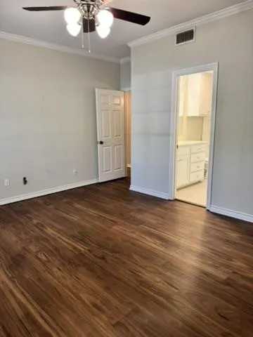 Unfurnished bedroom with ornamental molding, dark wood finished floors, ceiling fan, and ensuite bath