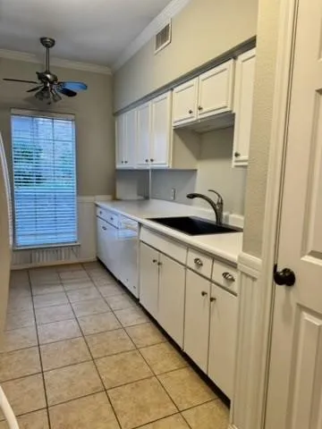 Kitchen featuring white cabinets, crown molding, a ceiling fan, light countertops, and wainscoting