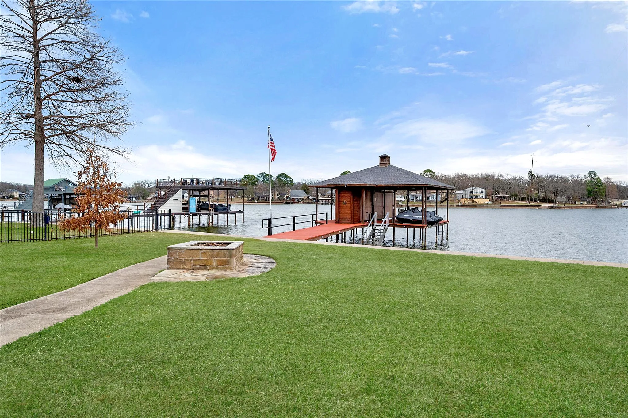 Dock with boat lift, a lawn, and an outdoor fire pit