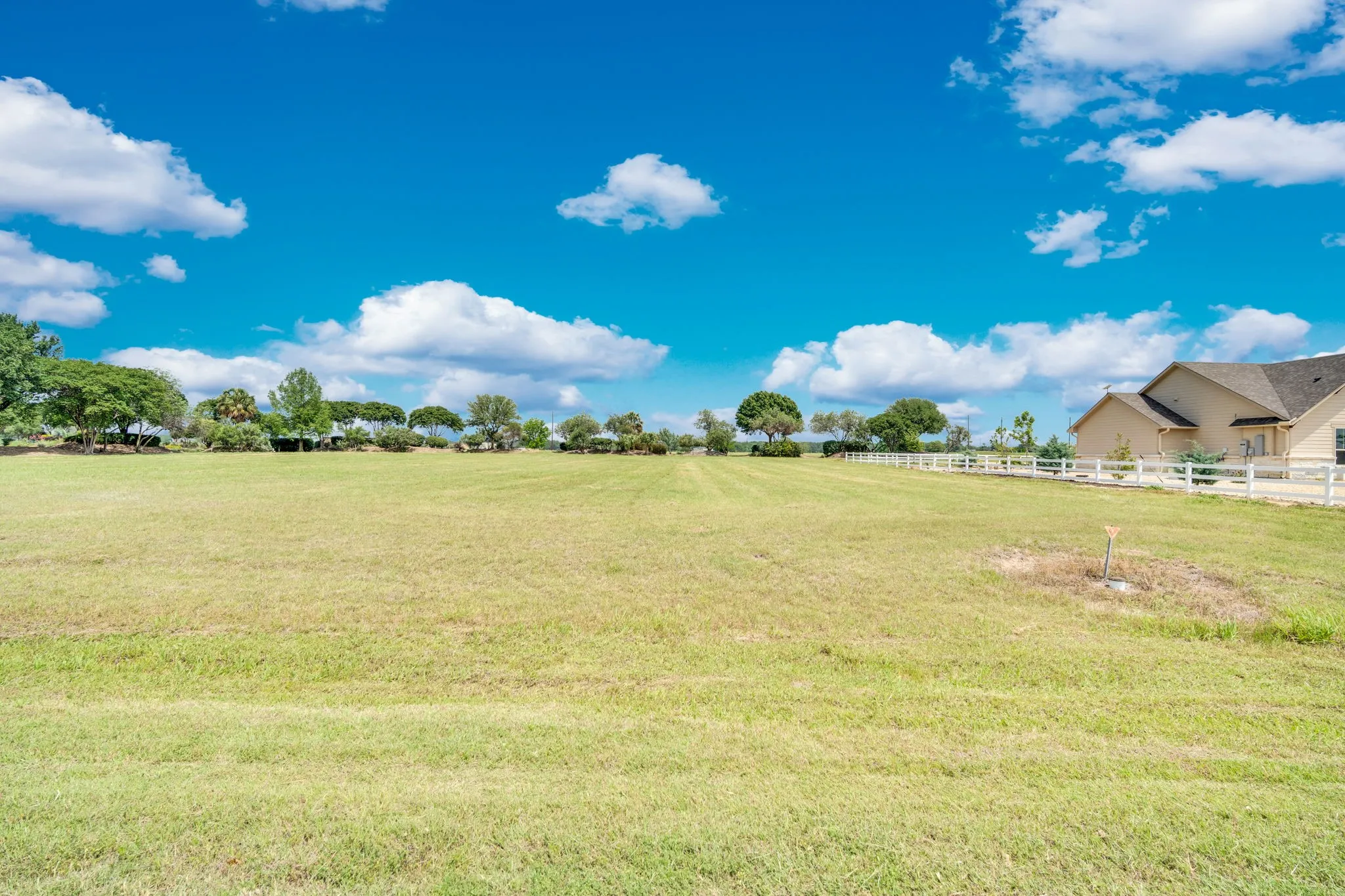 Expansive green field featuring a partially visible residence with a white fence