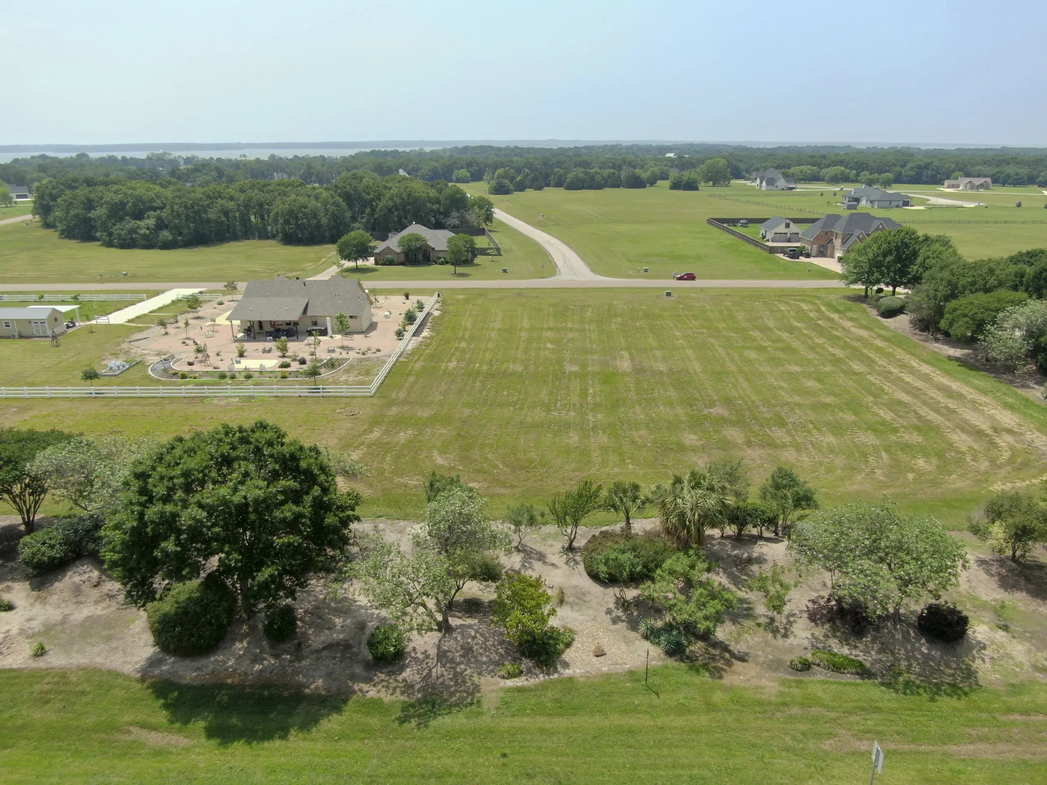 Expansive land parcel featuring a vast green space, established trees, a distant body of water, and surrounding residential properties