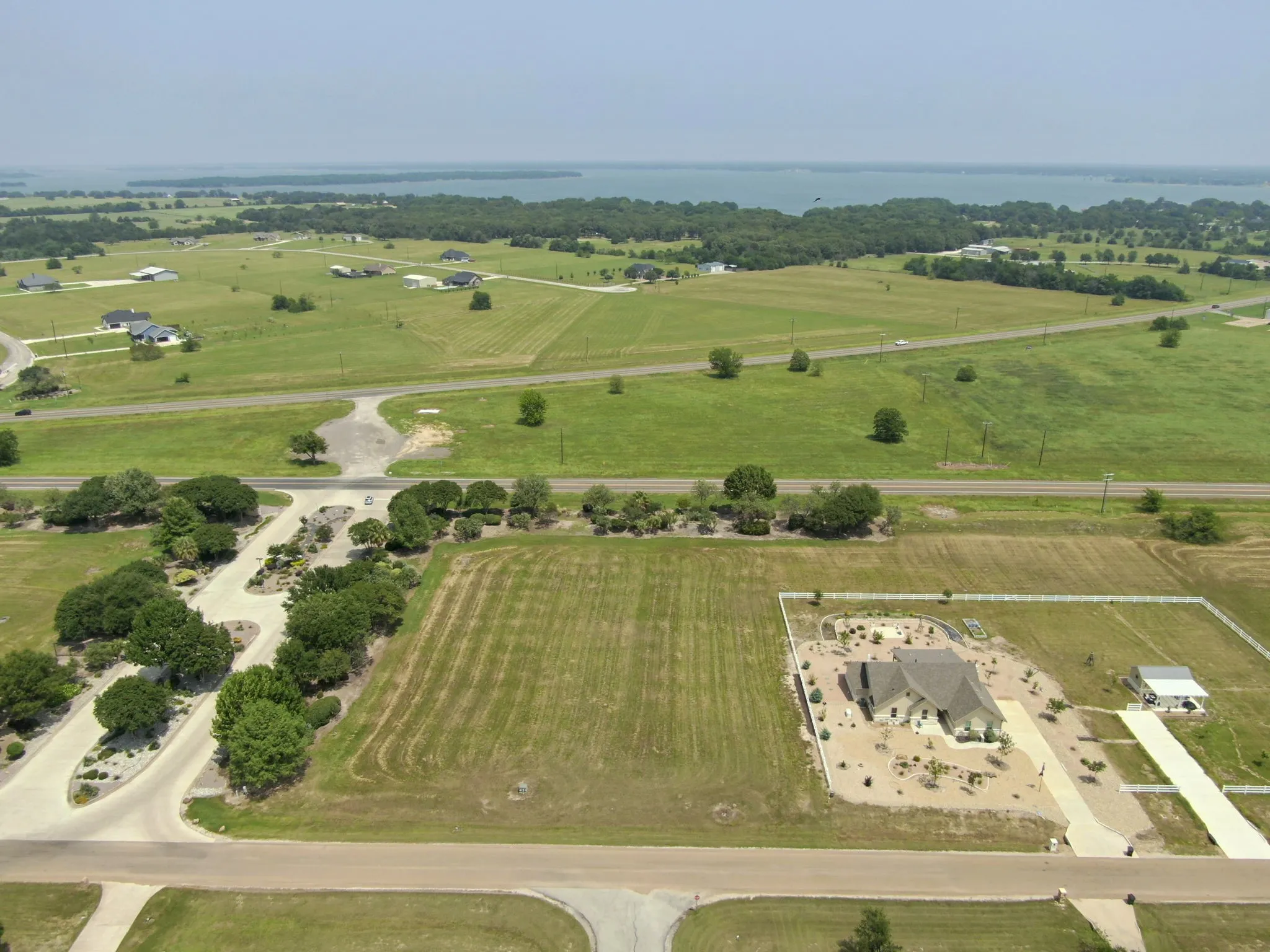 Aerial perspective showcasing a single-story residence with a light-colored exterior and dark roof, situated on a large parcel of land