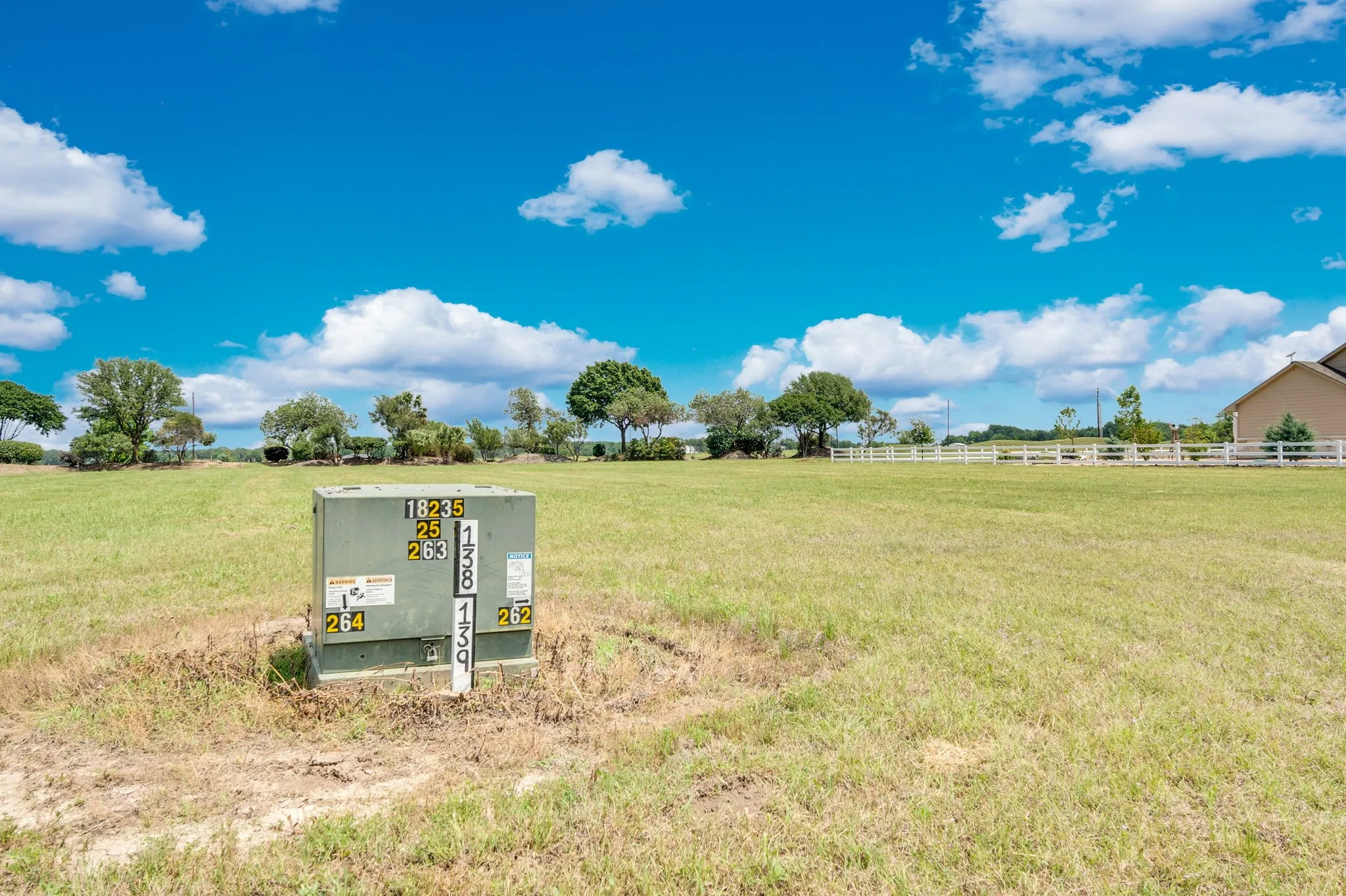 Expansive grassy lot featuring mature trees lining the perimeter and a white perimeter fence