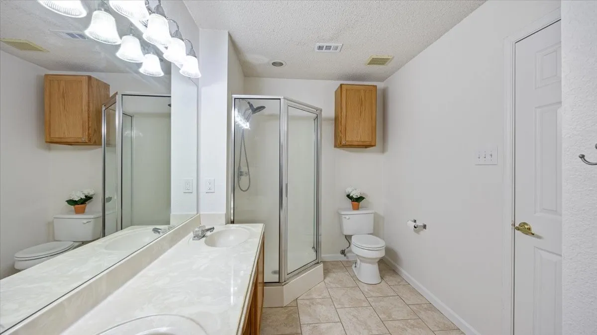 Bathroom featuring a dual vanity with integrated sinks and a large mirror, a corner glass-enclosed shower, and a toilet