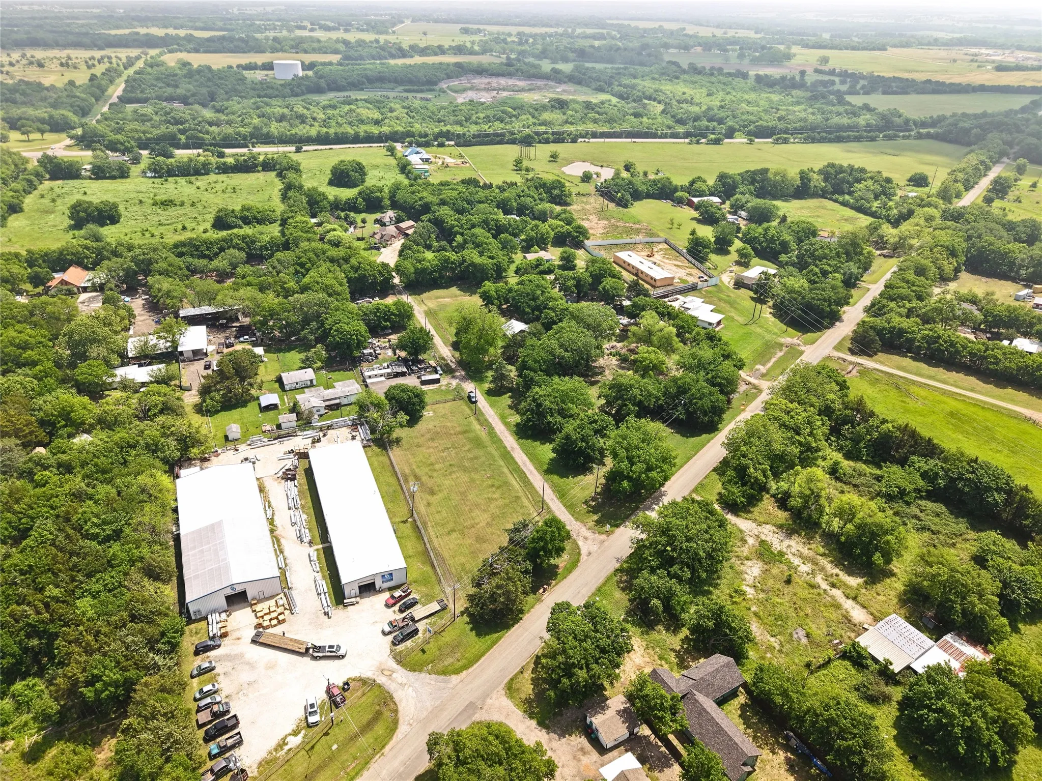 Aerial depiction of a landscape featuring two large industrial-style buildings with light-colored roofs, surrounded by extensive green areas and scattered trees