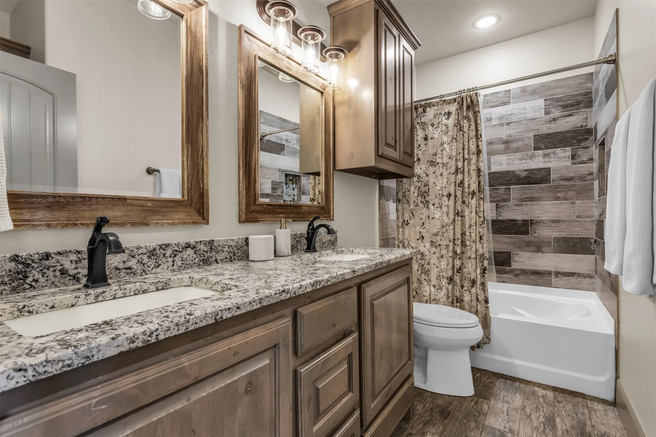 Full bathroom featuring double vanity, shower / bathtub combination with curtain, and dark wood-style floors