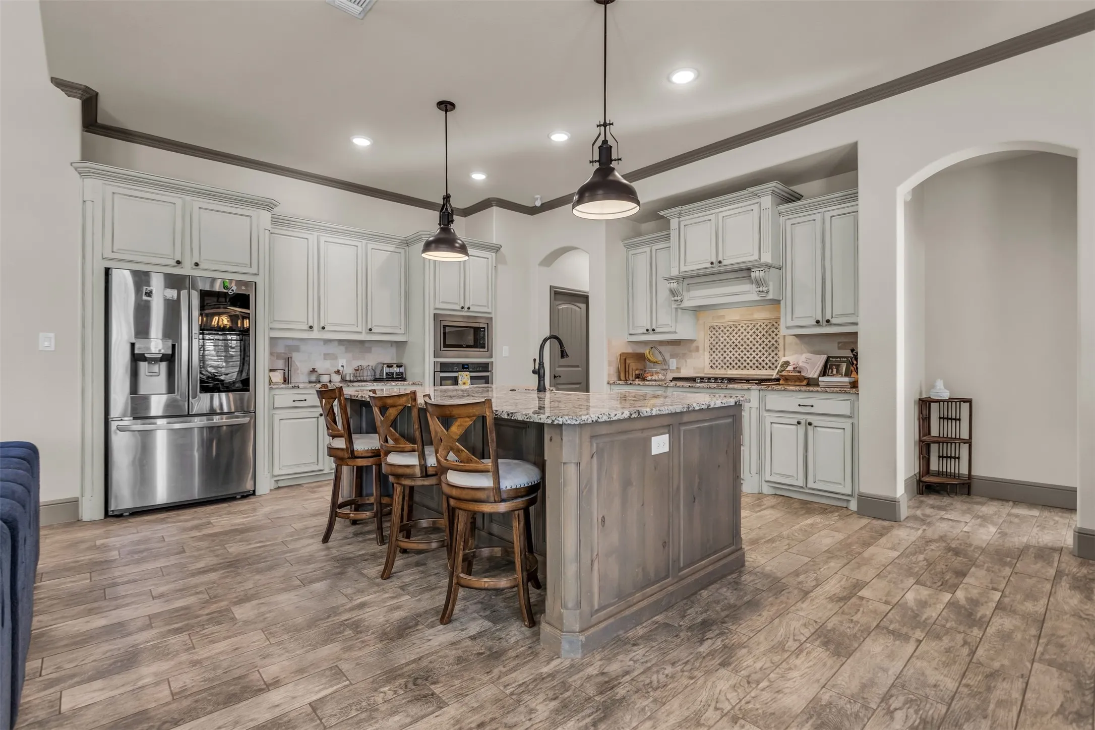 Kitchen featuring stainless steel appliances, crown molding, a center island with sink, decorative light fixtures, and backsplash