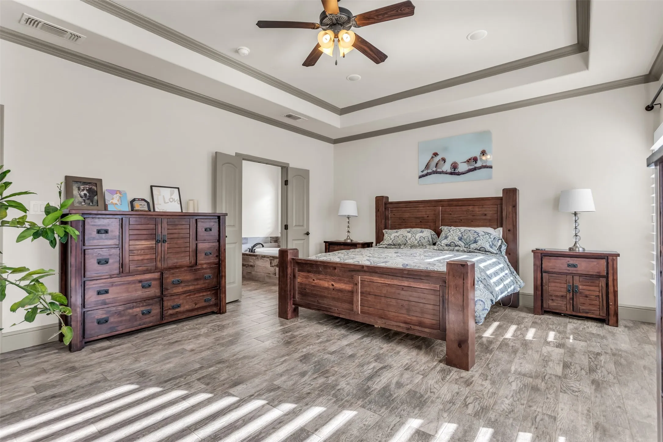 Bedroom featuring ornamental molding, light wood-style flooring, a raised ceiling, and ceiling fan